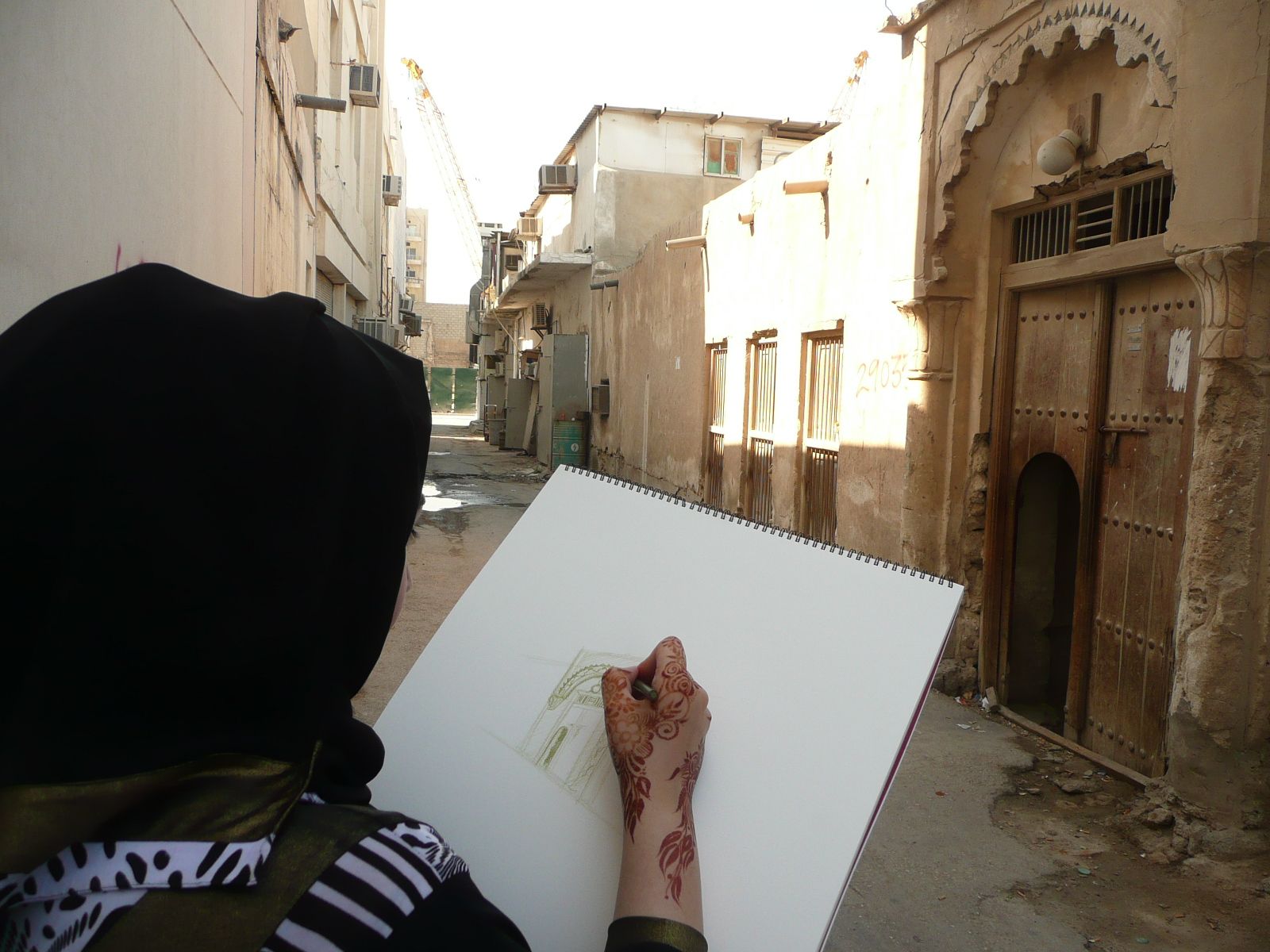 View over a woman's shoulder as she sketches a historic Doha street on an artists' sketchpad during Qatar-Uk 2013.