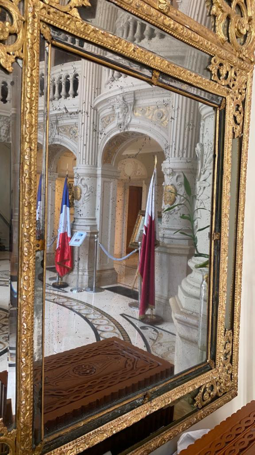 Reflection in a gold-framed mirror of the France and Qatar flags side by side at the  Qatar Embassy in France.