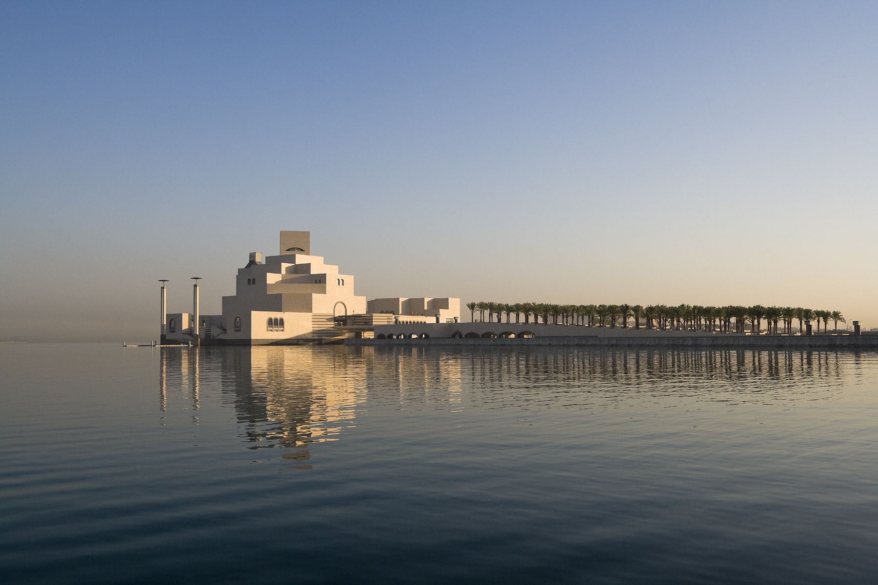 The iconic angular white stone building of the Museum of Islamic art, seen from across the water from a distance.