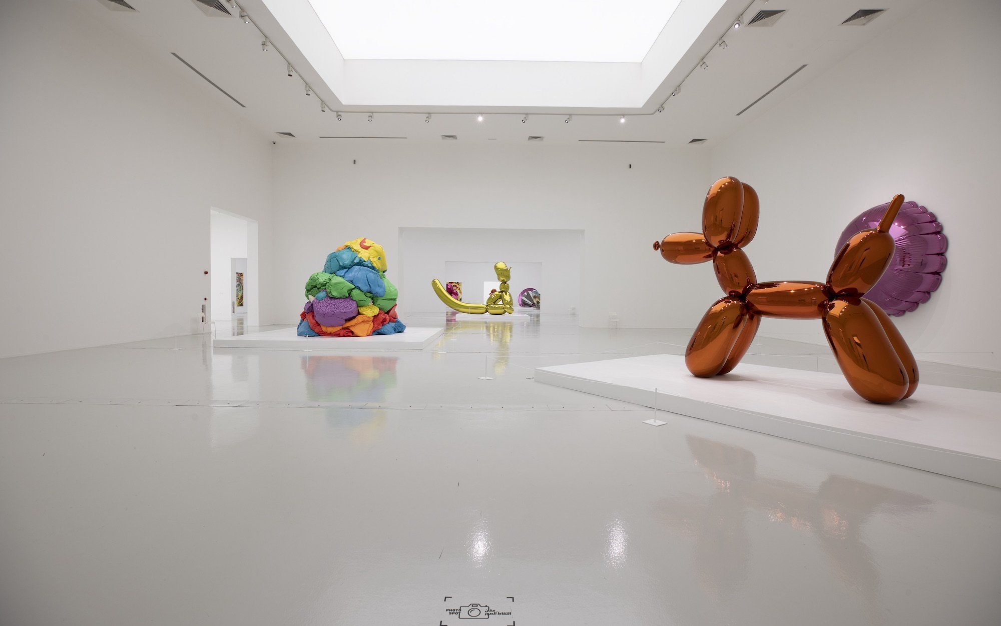 Bright gallery space with white walls and floor with colourful Jeff Koons sculptures depicting giant balloon animals.