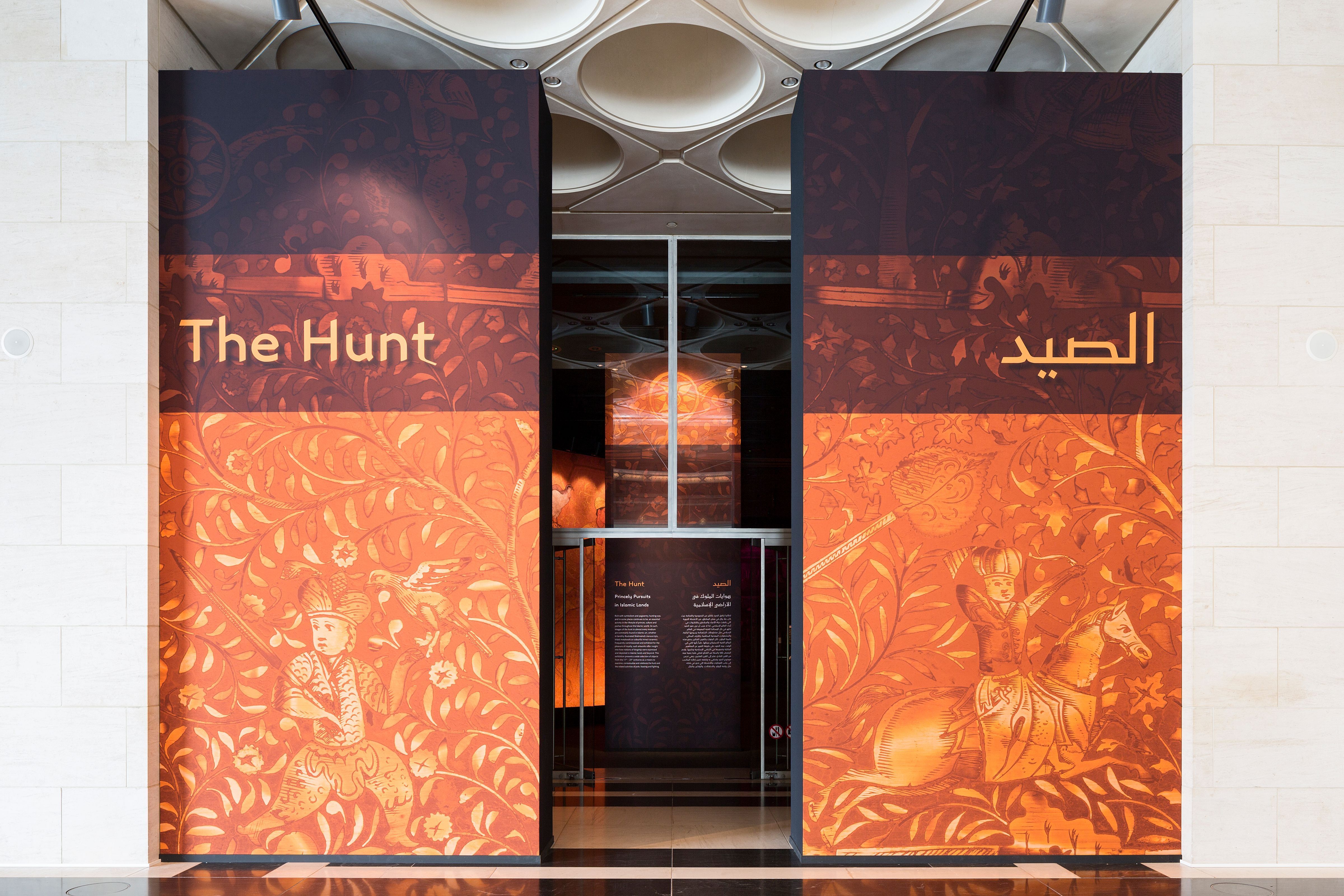 Entrance to an exhibition between 2 orange floor to ceiling panels depicting traditional Turkish illustrations and text.