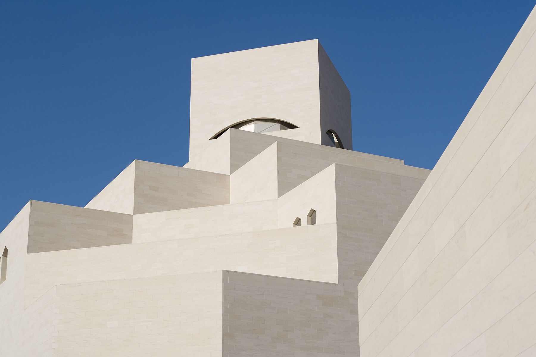 The unique architecture of the Museum of Islamic Art, with tiered blocks of pale stone against a bright blue sky.