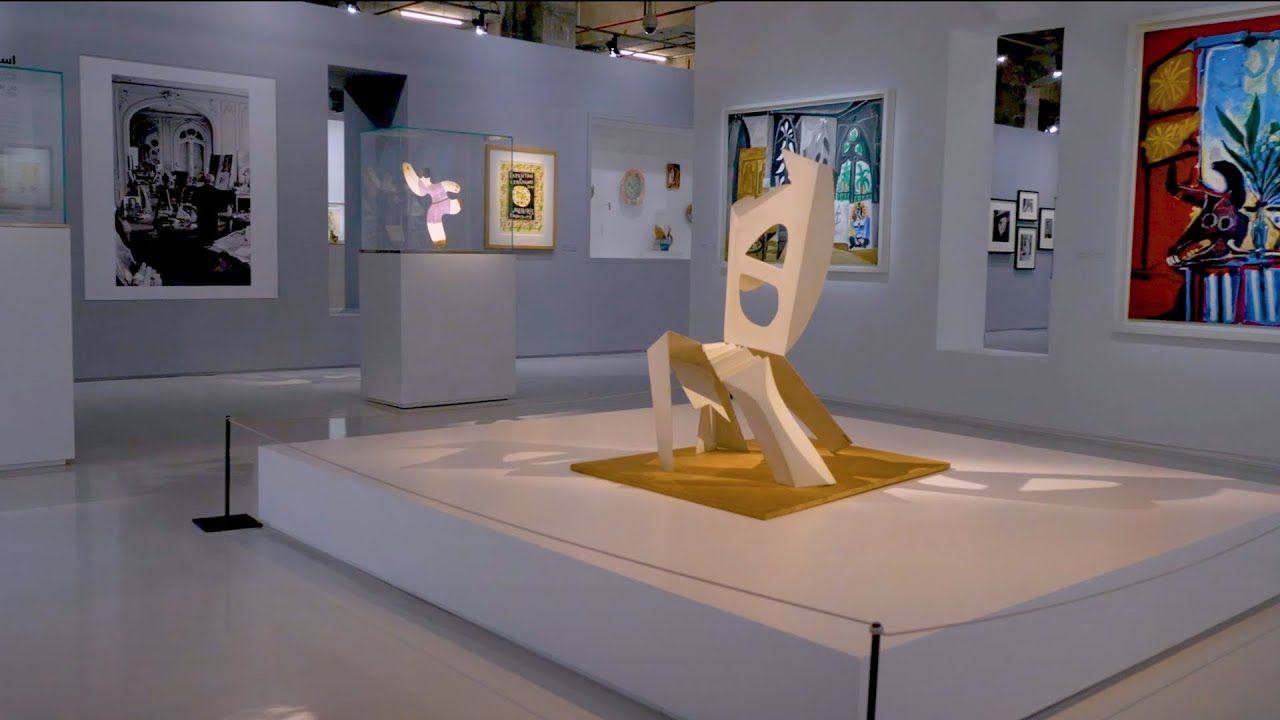 Contemporary white sculpture by Picasso on display in a gallery space with painted artworks displayed on the walls.