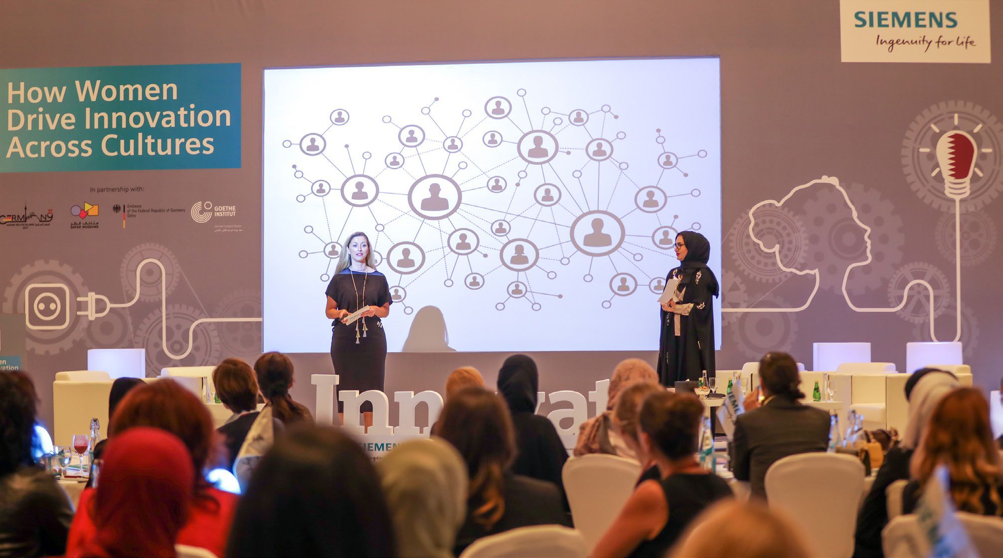Two women on stage give a presentation to an audience as part of Qatar-Germany 2017.