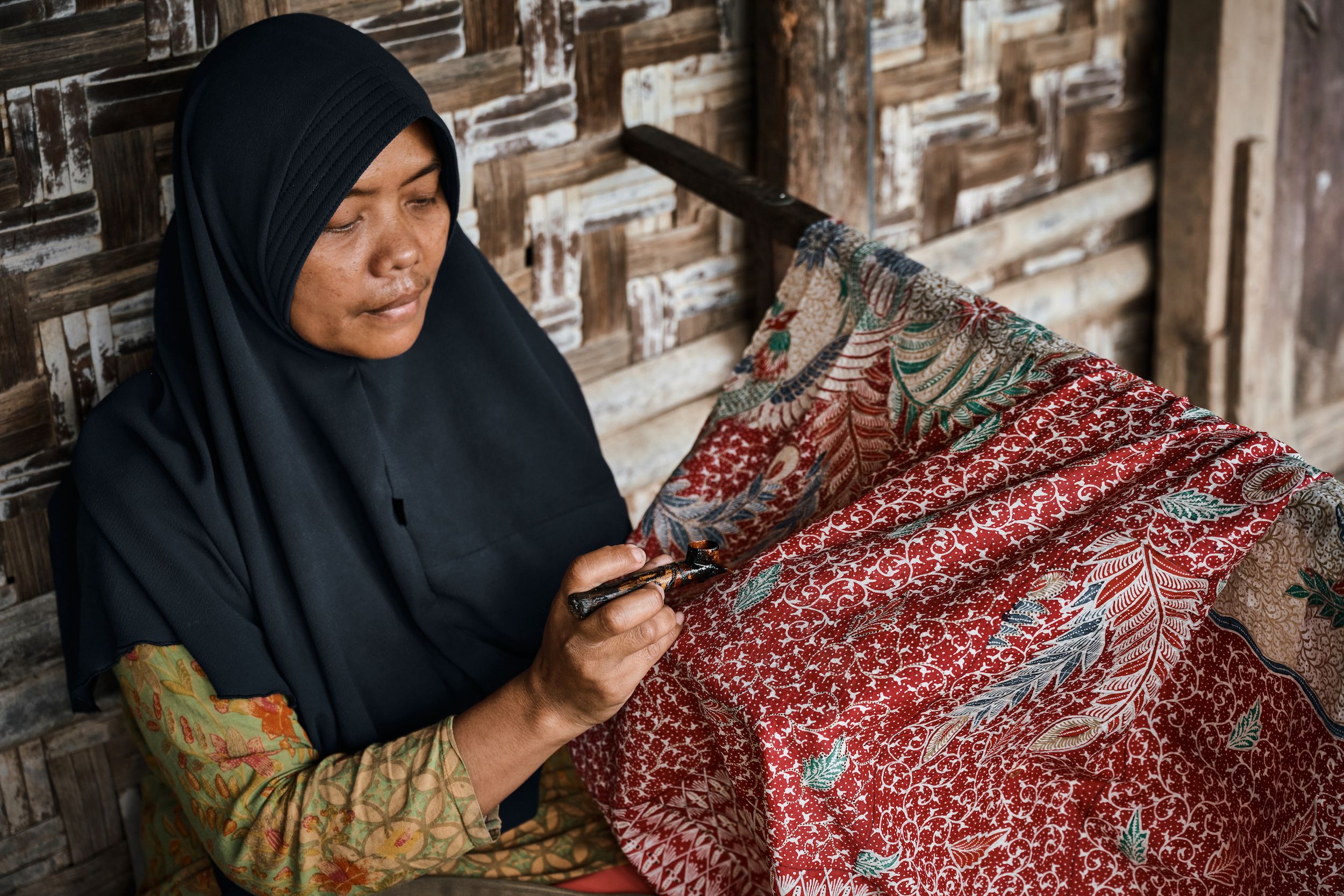Indonesian woman creating an elaborate Batik design on fabric with red and blue colours.