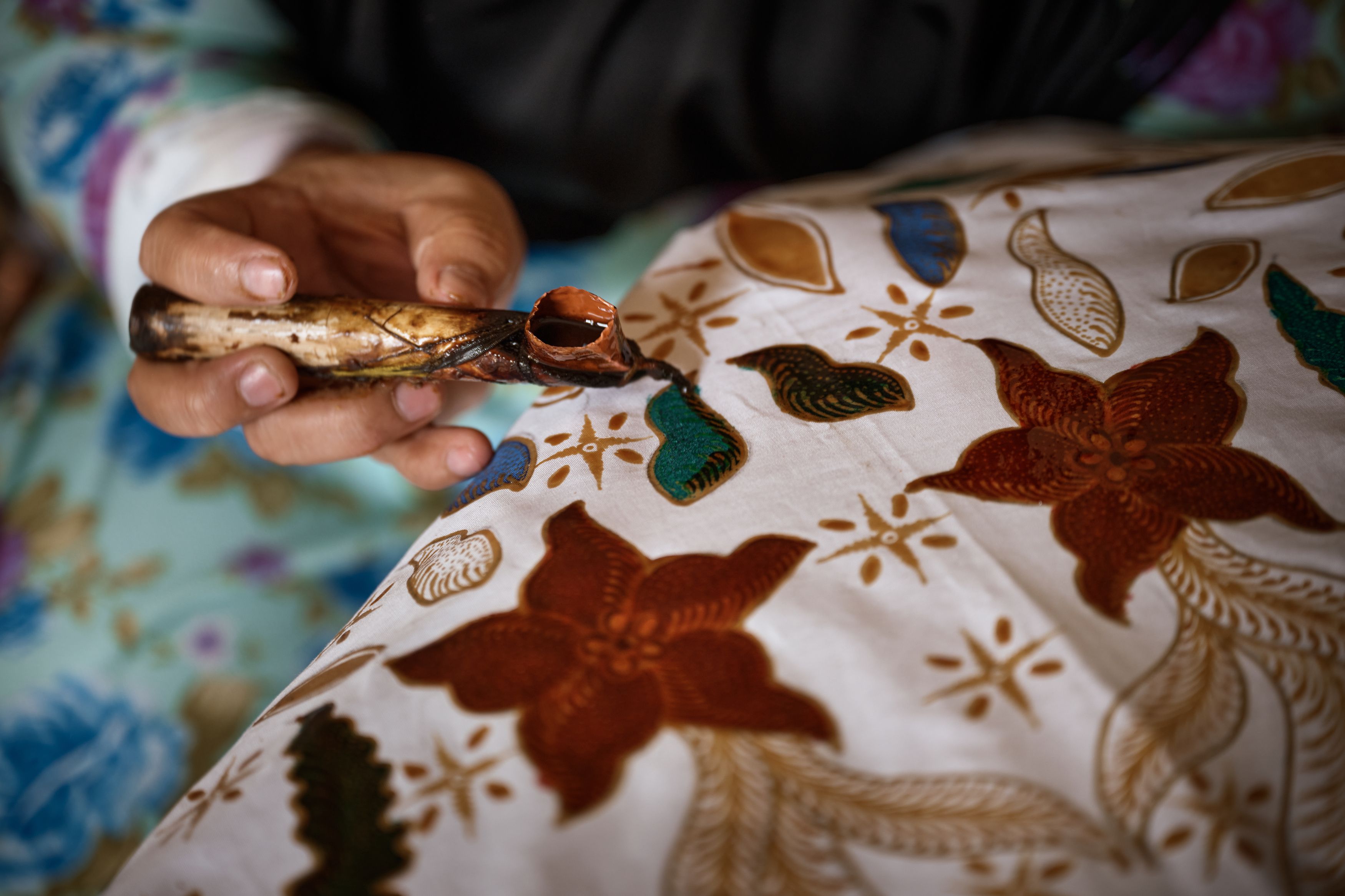 Close-up view of a hand painting a traditional Indonesian Batik design onto fabric.