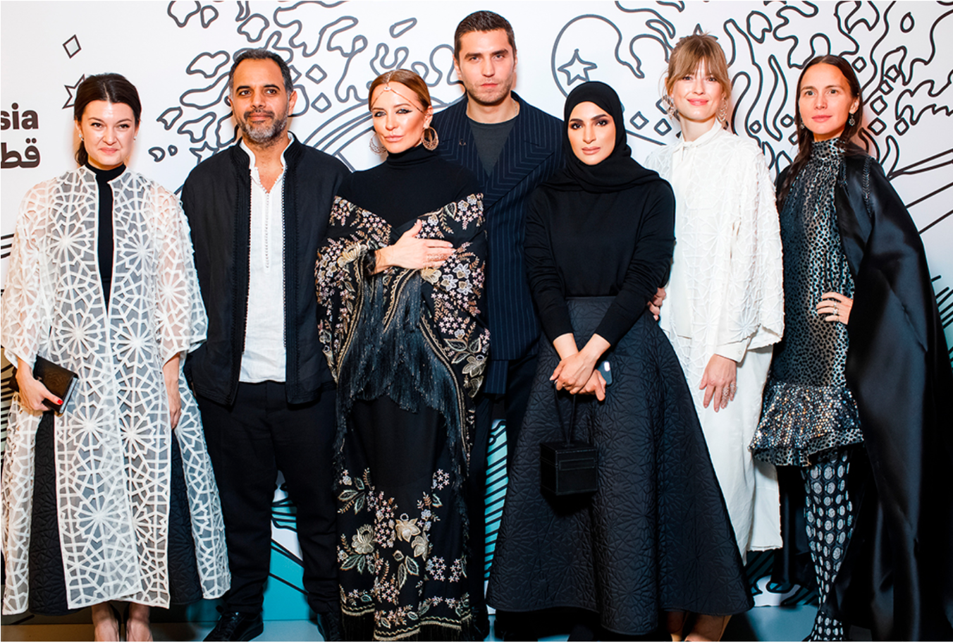 A fashionable group of men and women pose side by side, smiling at Qatari Fashion and Jewellery Art in Moscow.