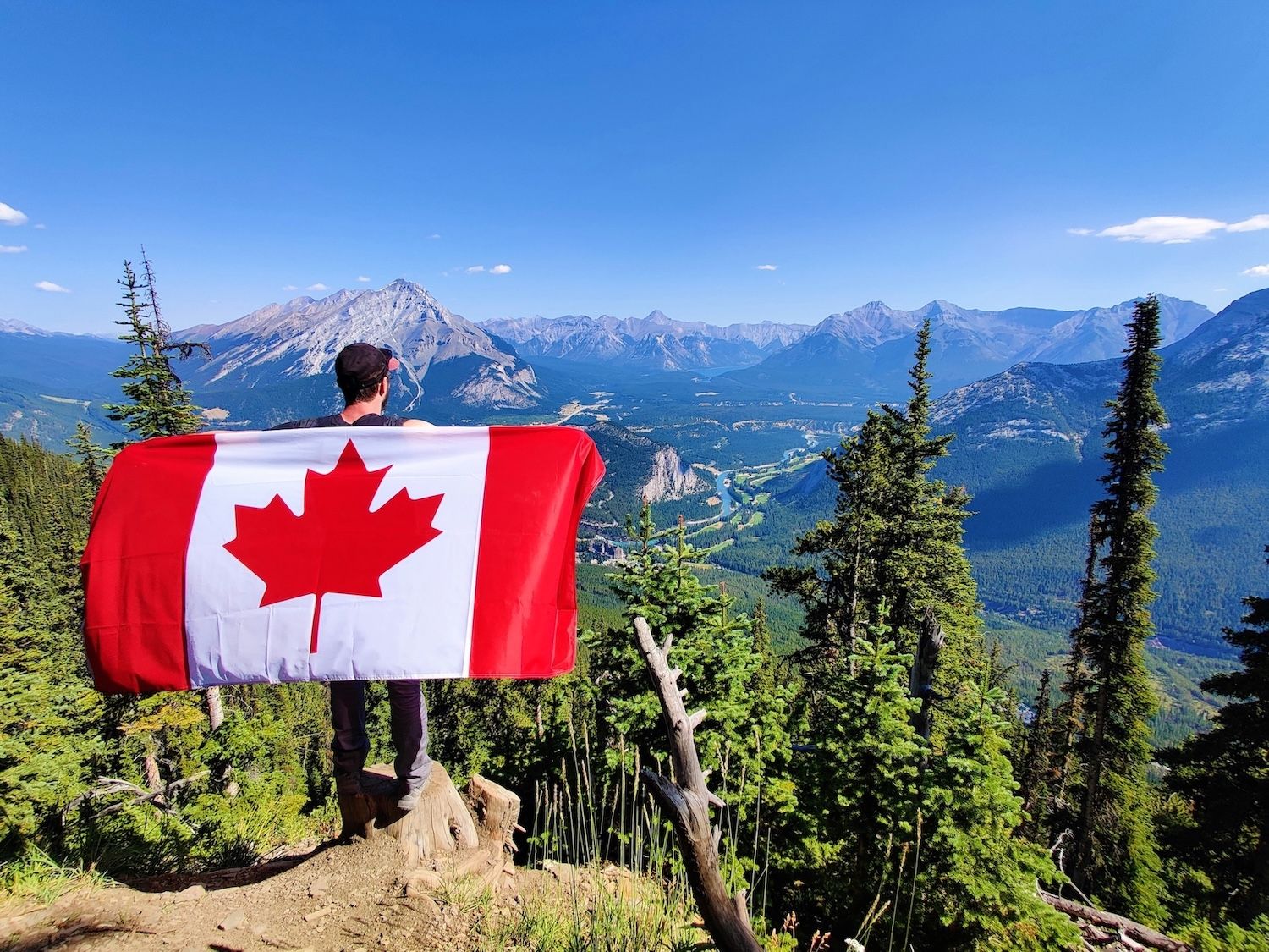 A person standing on a mountain peak while holding the Flag of Canada, also known as the Maple Leaf Flag.