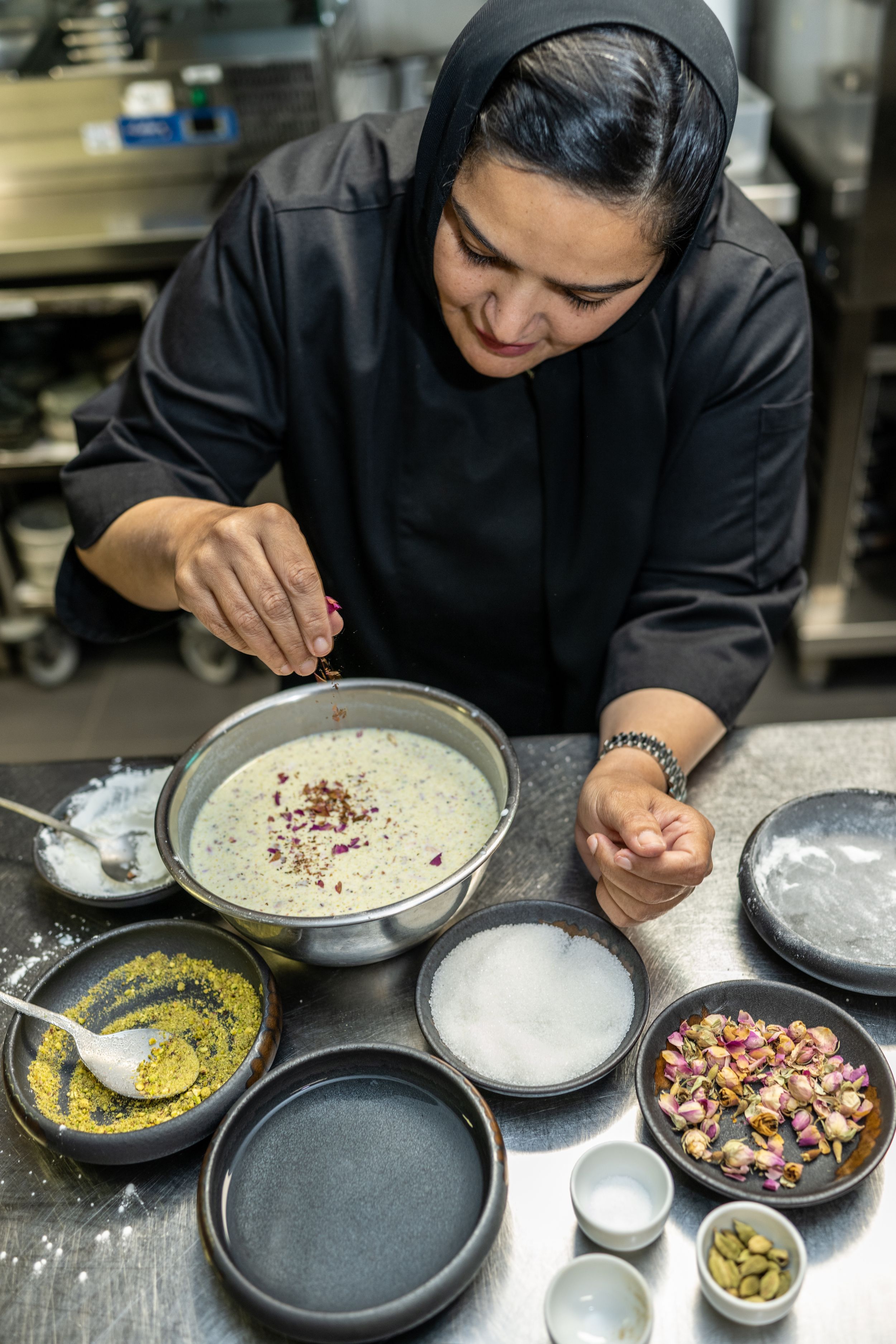 Renowned Qatari Chef Noof adds spices to a bowl, surrounded by ingredients in her professional kitchen.