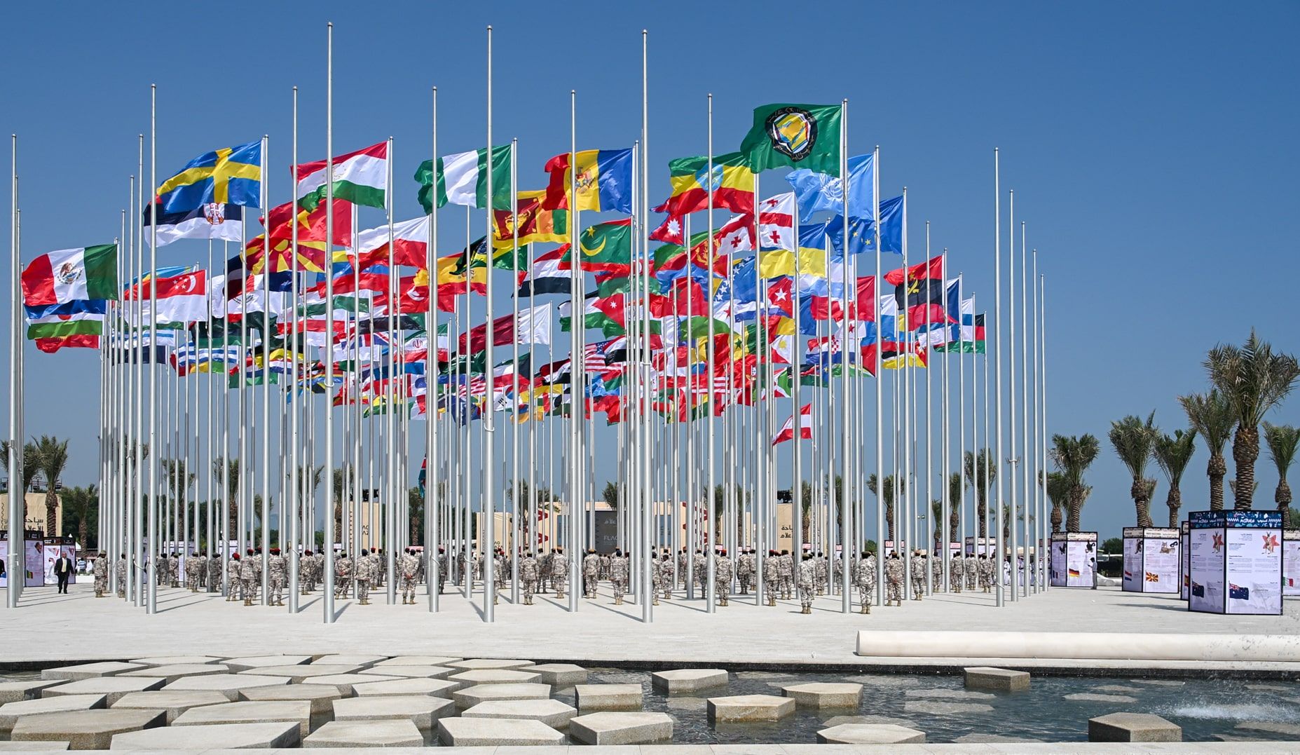 The Flag Plaza in Doha, with a water feature in the foreground and 120 flag poles with international flags flying.