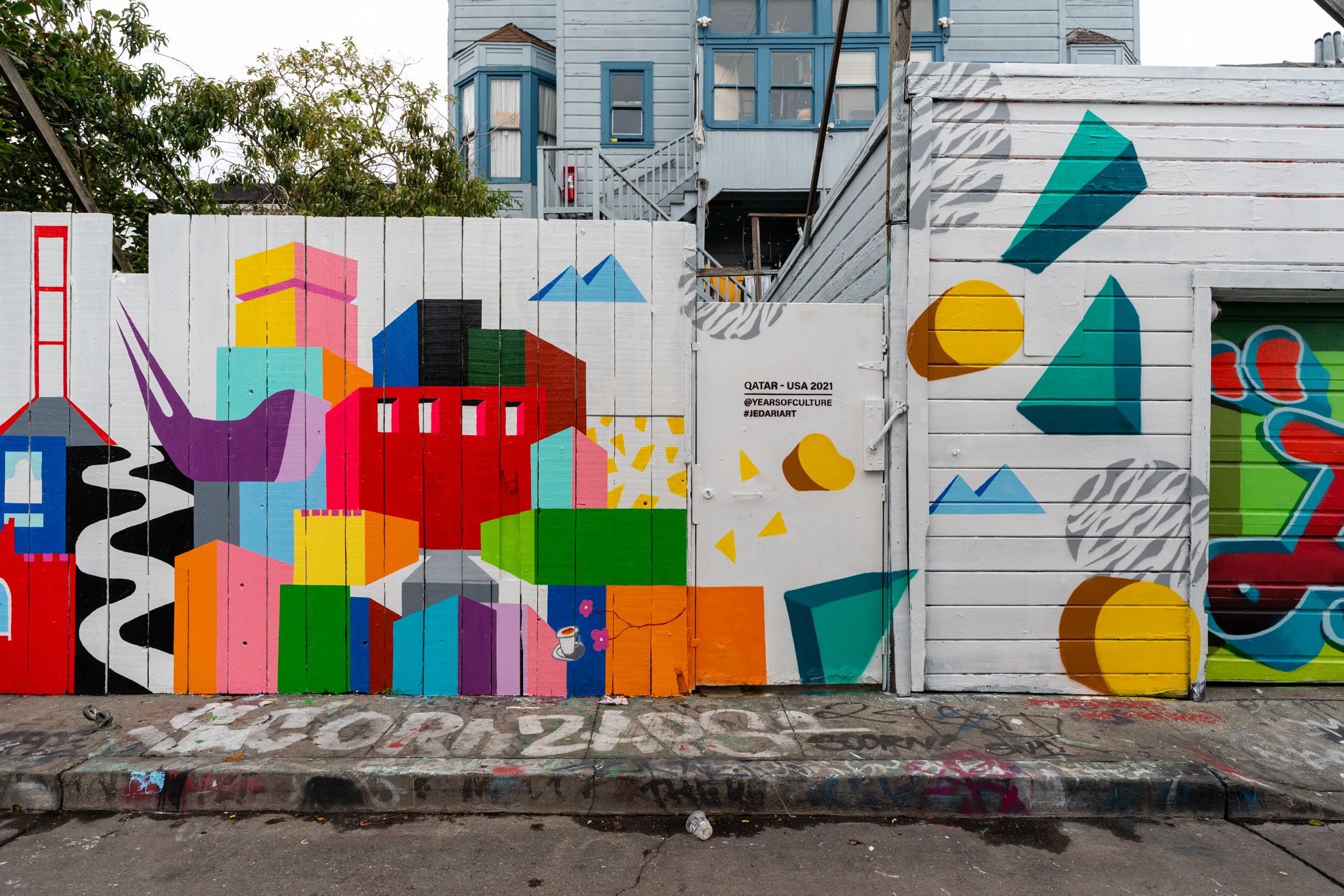 Bold graphic mural painted on a white wooden fence during JEDARIART in San Francisco.