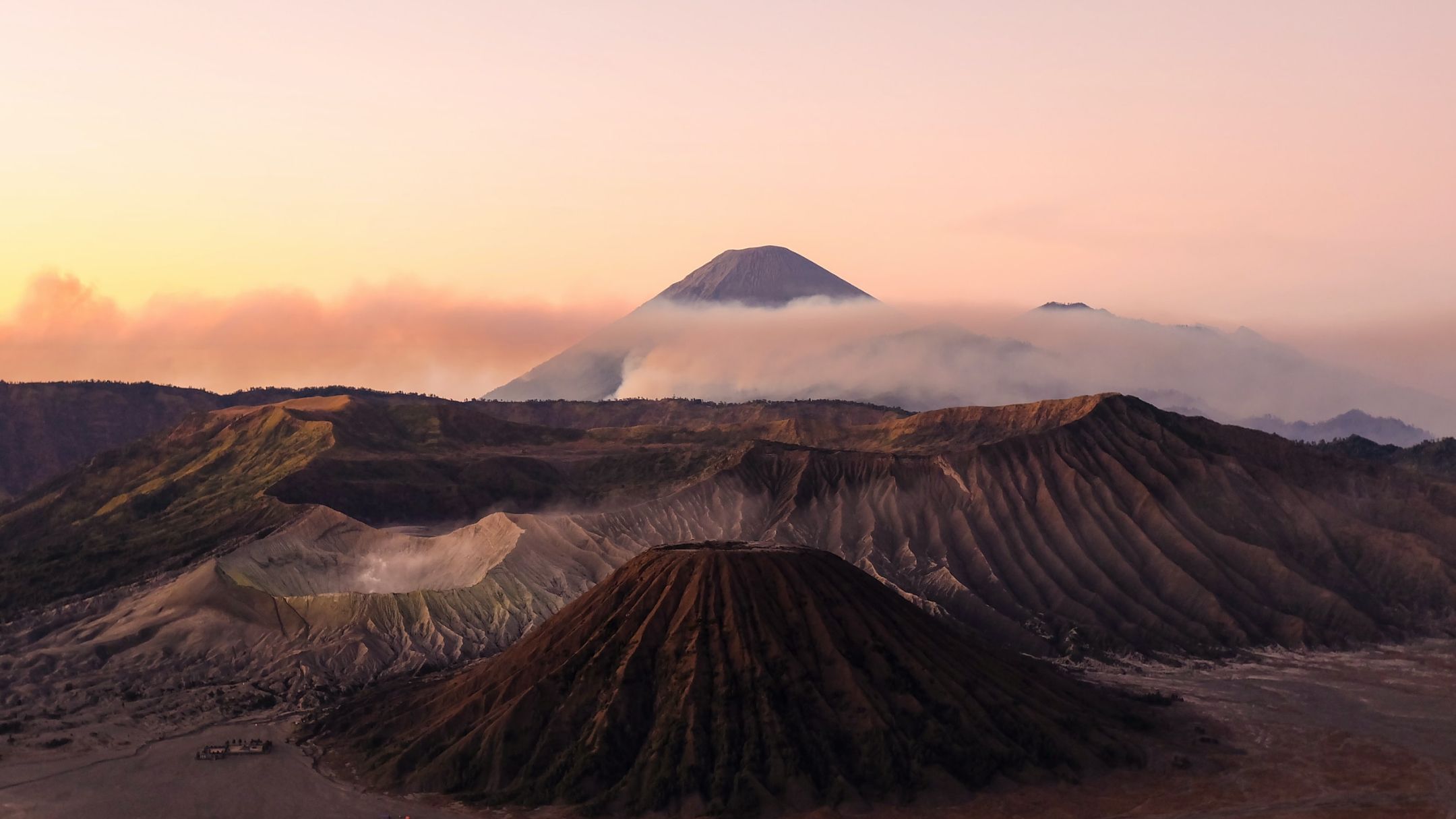 Volcanic landscape in Indonesia, rocky volcanoes surrounded by misty clouds against a sunset sky.