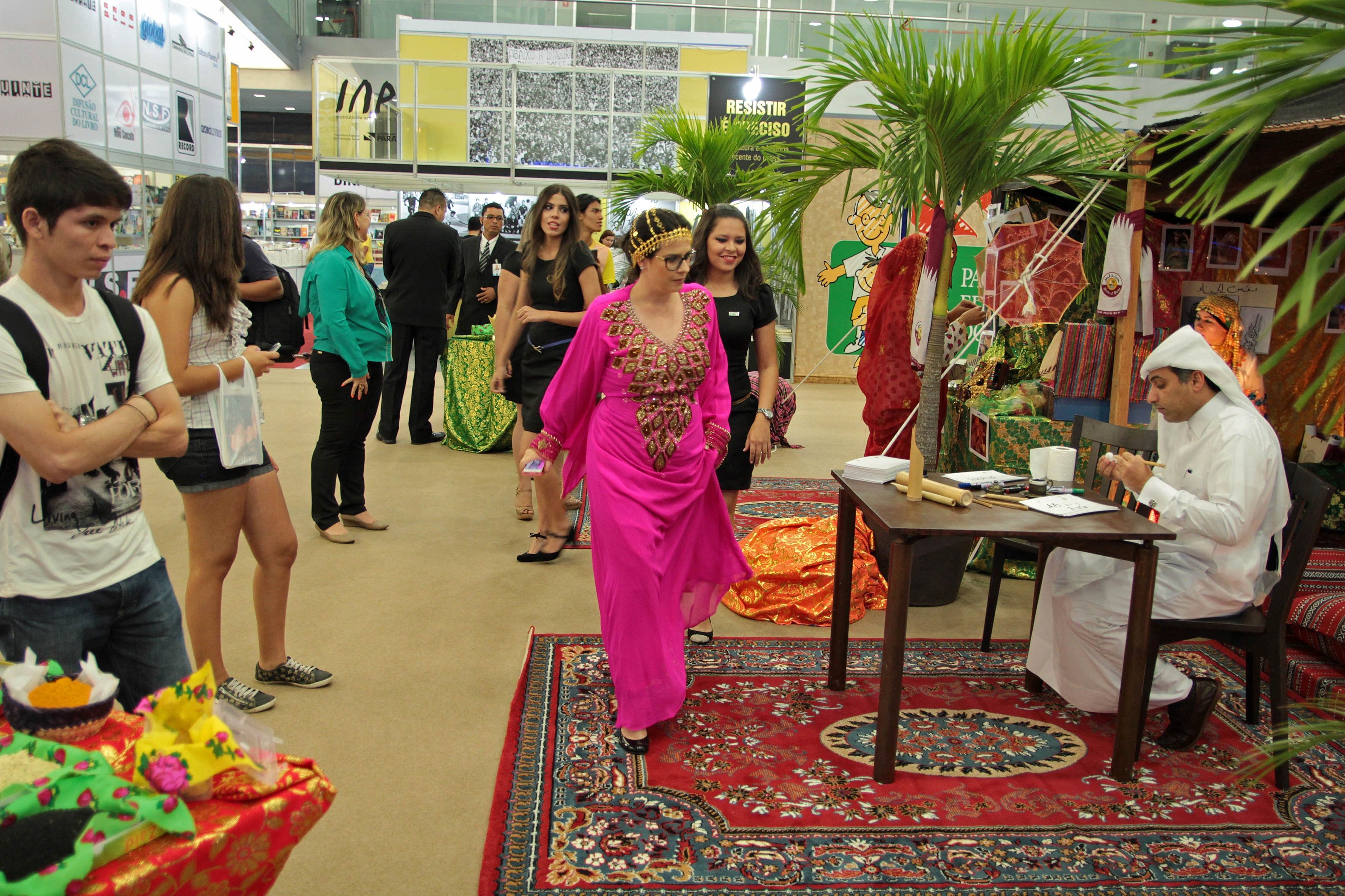 The Pan-Amazon book fair during Qatar-Brazil 2014, with an author sitting at a table and groups of people walking by.