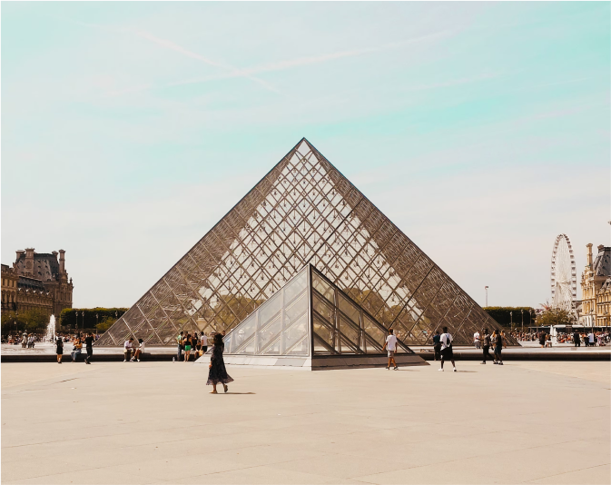 Iconic view of the Louvre museum in Paris, an open square with the famous glass pyramid at the centre against a blue sky.