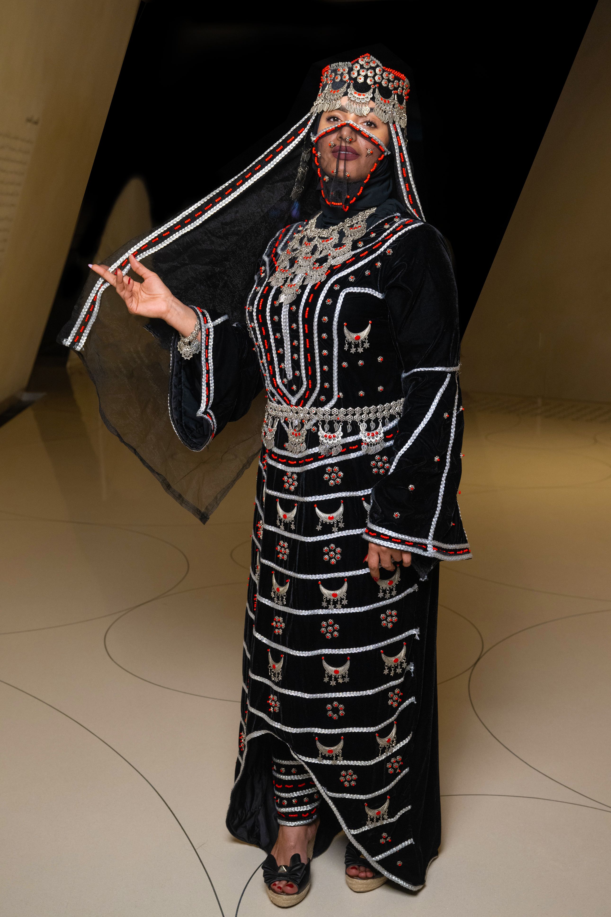 Woman modelling a traditional Yemeni velvet dress worn with a traditional silver necklace, veil and headpiece.