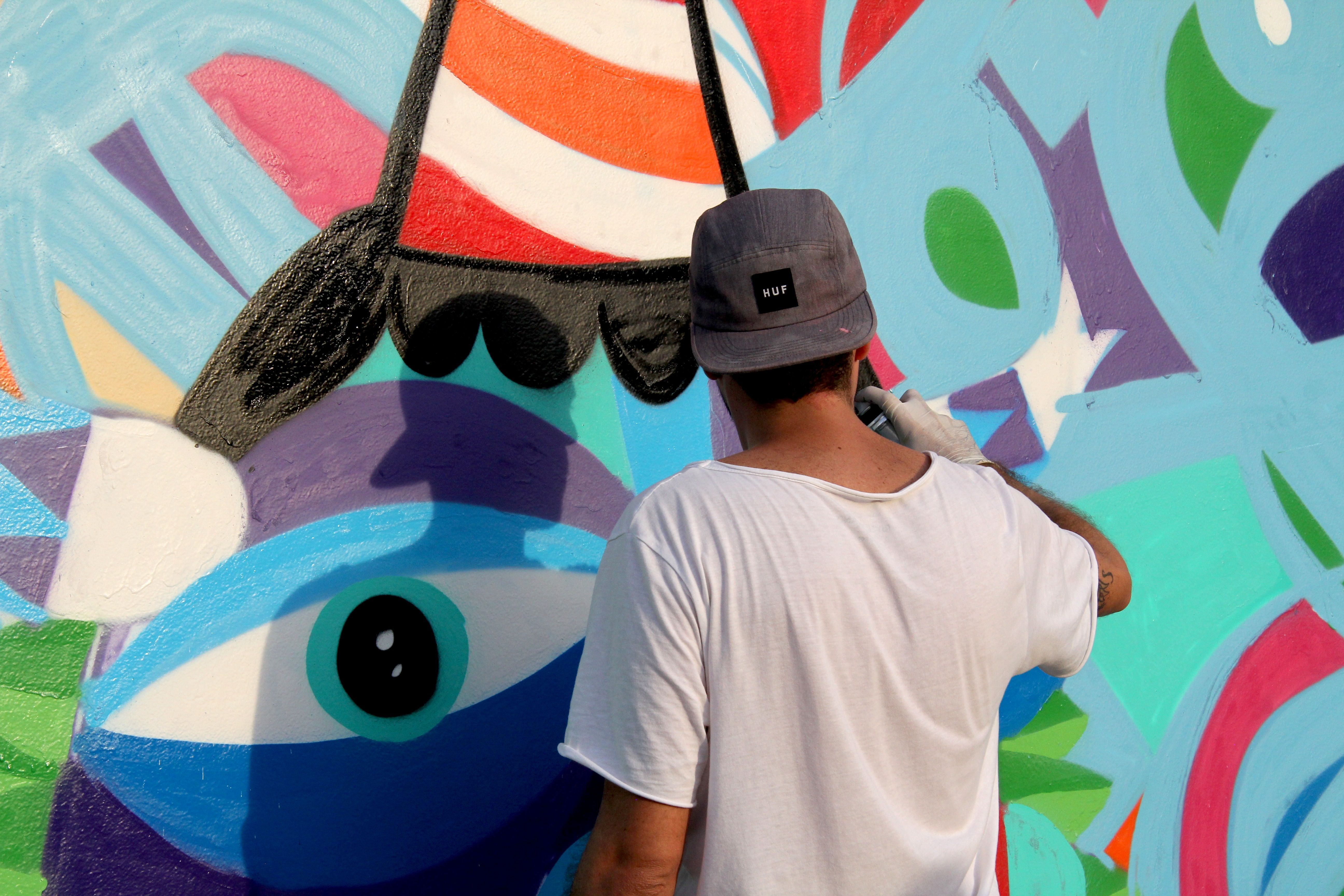 A man wearing a baseball cap and white t-shirt paints a colourful mural with spray paint during Qatar-Brazil 2014. 