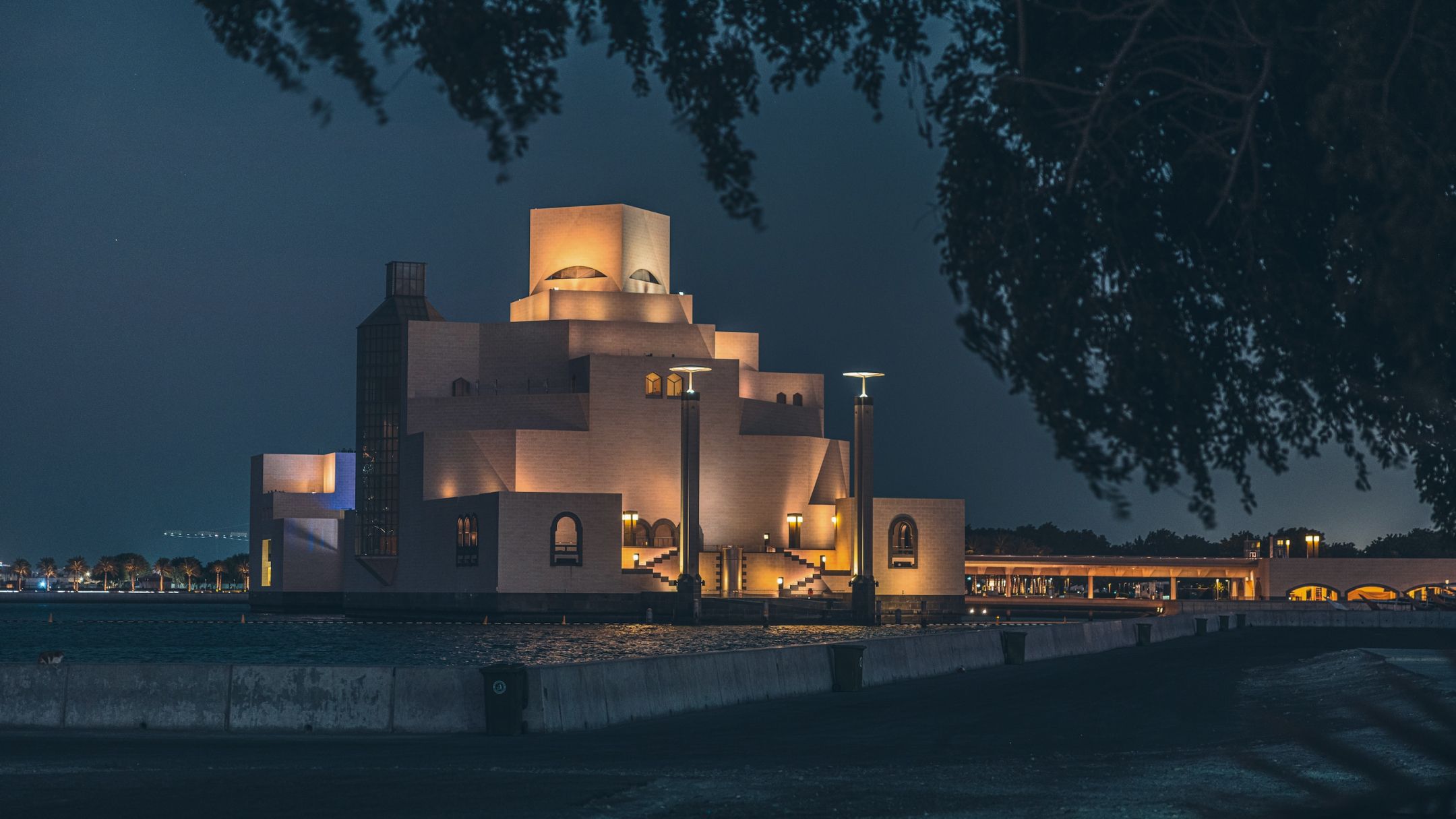 The elegant architecture of the Museum of Islamic Art in Qatar, illuminated with a warm glow against the night sky.