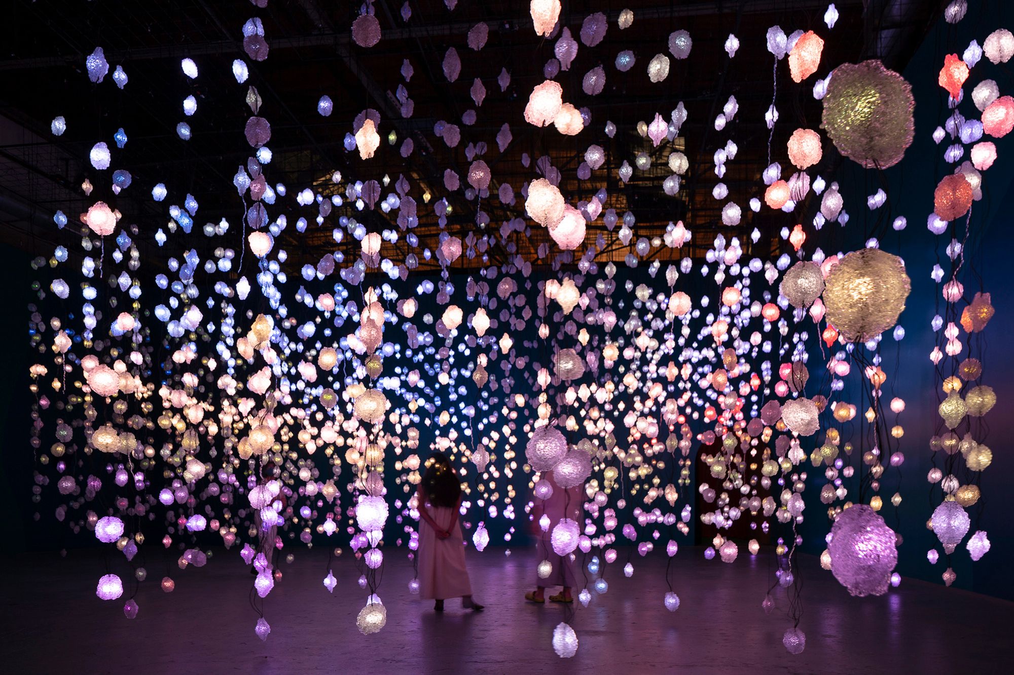 A dark gallery space filled with lights hung on vertical cables, as part of the Pipilotti Rist exhibition in Qatar.