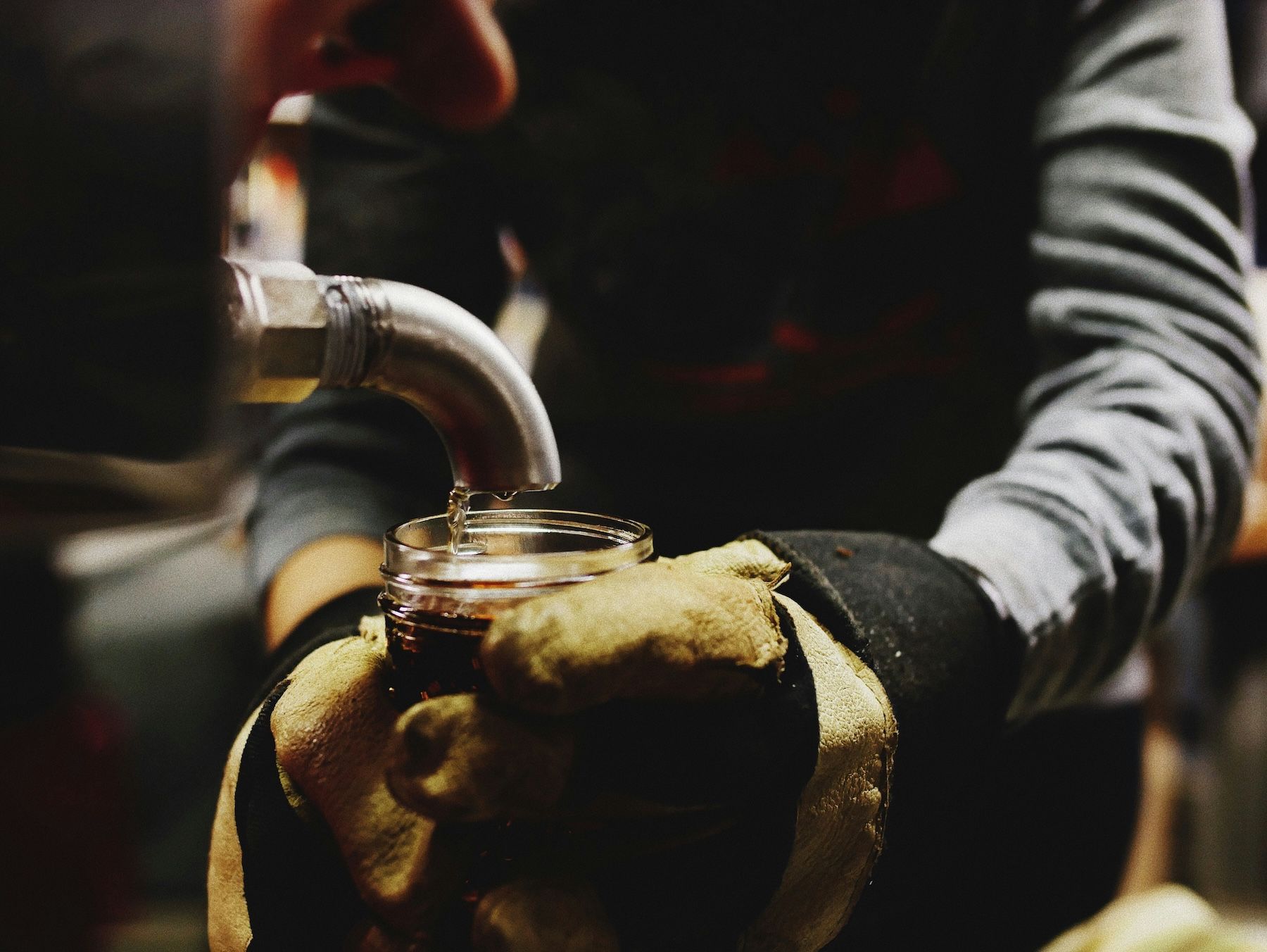 man collecting an example of maple syrup from an industrial tap in a sugar shack