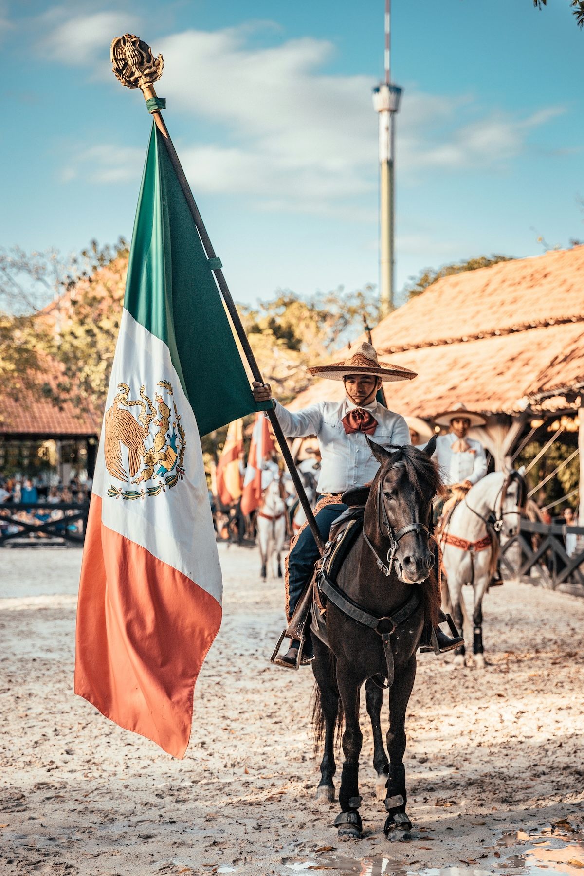 a charro, historical mexican horseman, riding a horse and carrying the flag of Mexico during a cultural event