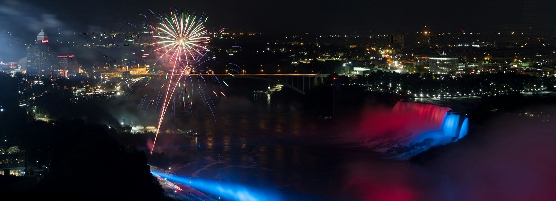 Niagara Falls illuminated at night, featuring a fireworks display over the Horseshoe Falls.