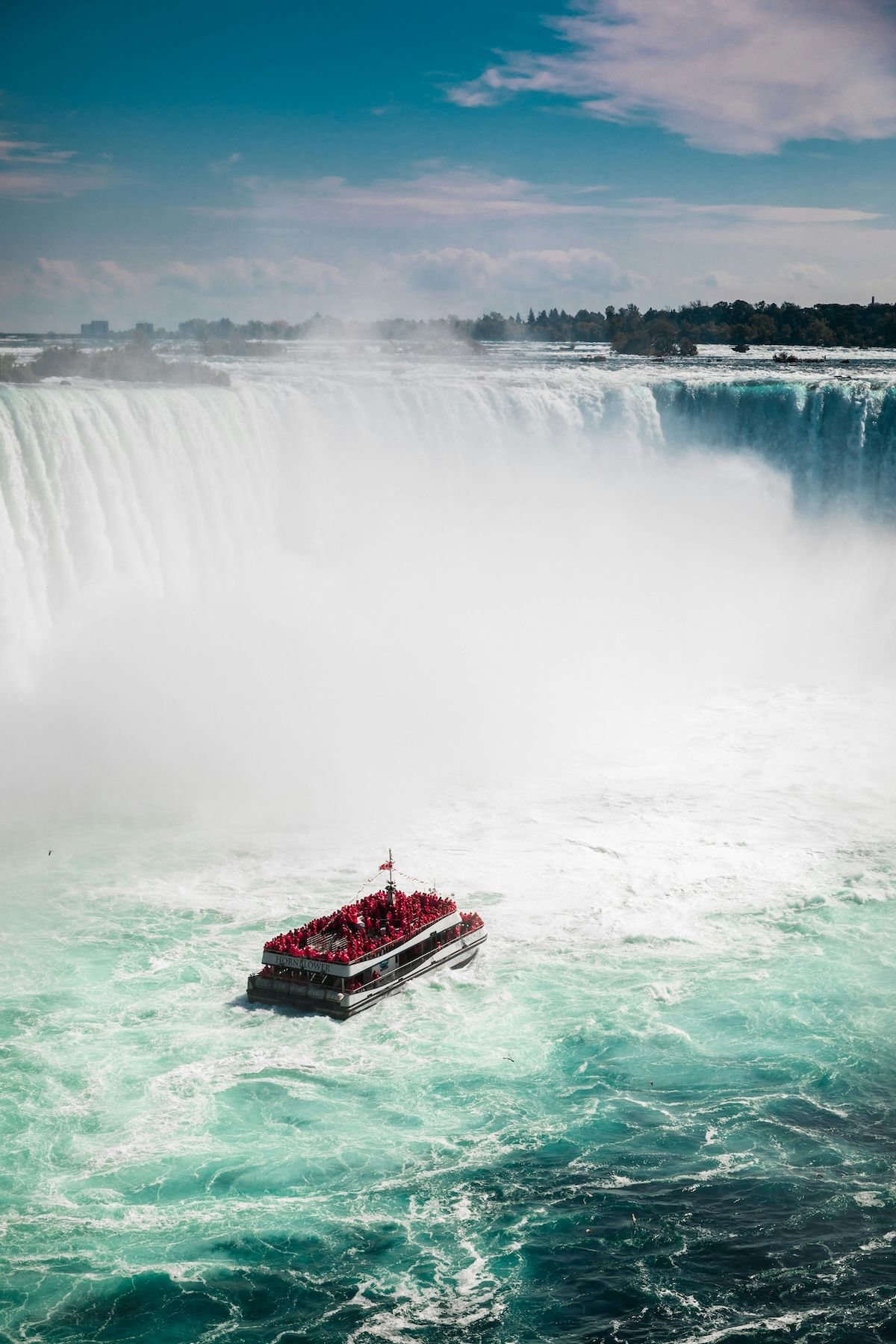 A tourist boat, likely the iconic Maid of the Mist or Hornblower Niagara Cruises, navigating the powerful waters at the base of Niagara Falls