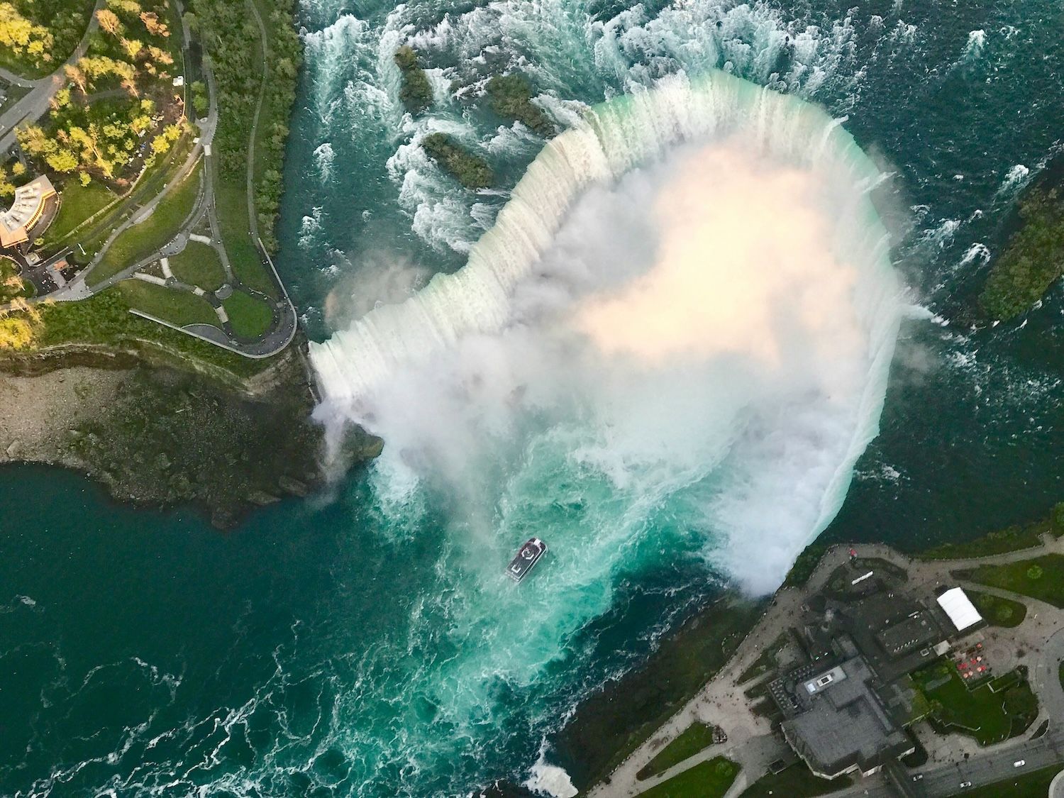 Aerial view of the Horseshoe Falls, the largest of the three waterfalls forming the Niagara Falls. A tourist boat is approaching the base of the falls.