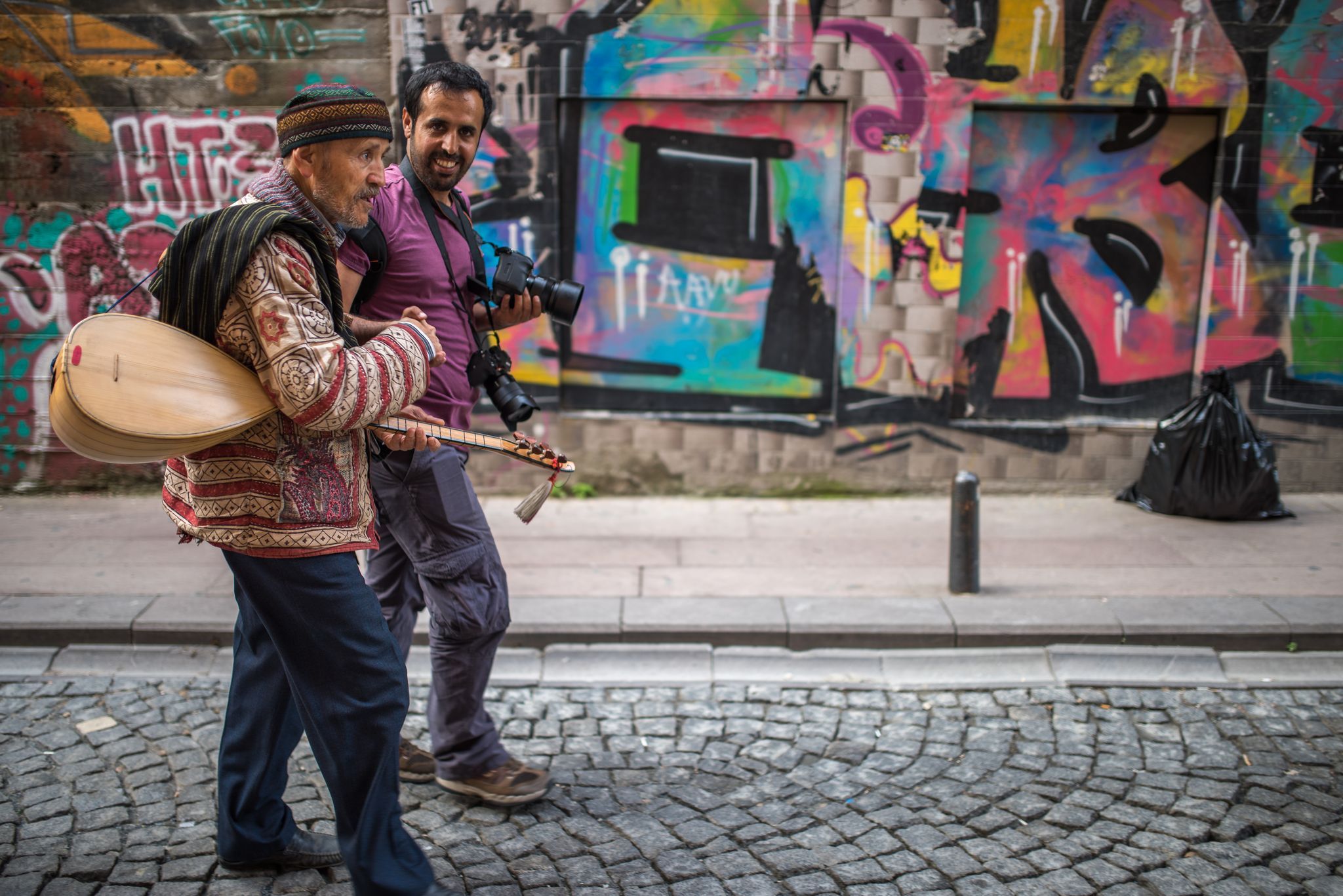 A photographer and a musician walk along a cobbled street, during the Qatar-Turkey 2015 photography exchange.