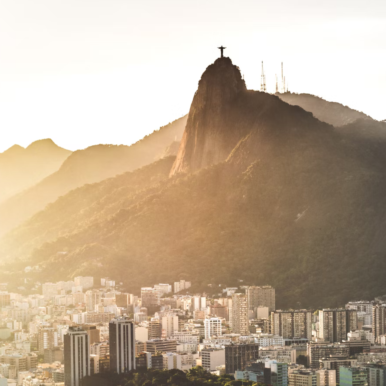 Sunrise over Rio de Janeiro in Brazil, with urban sprawl in front of hills and Christ The Redeemer statue on Mount Corcovado.