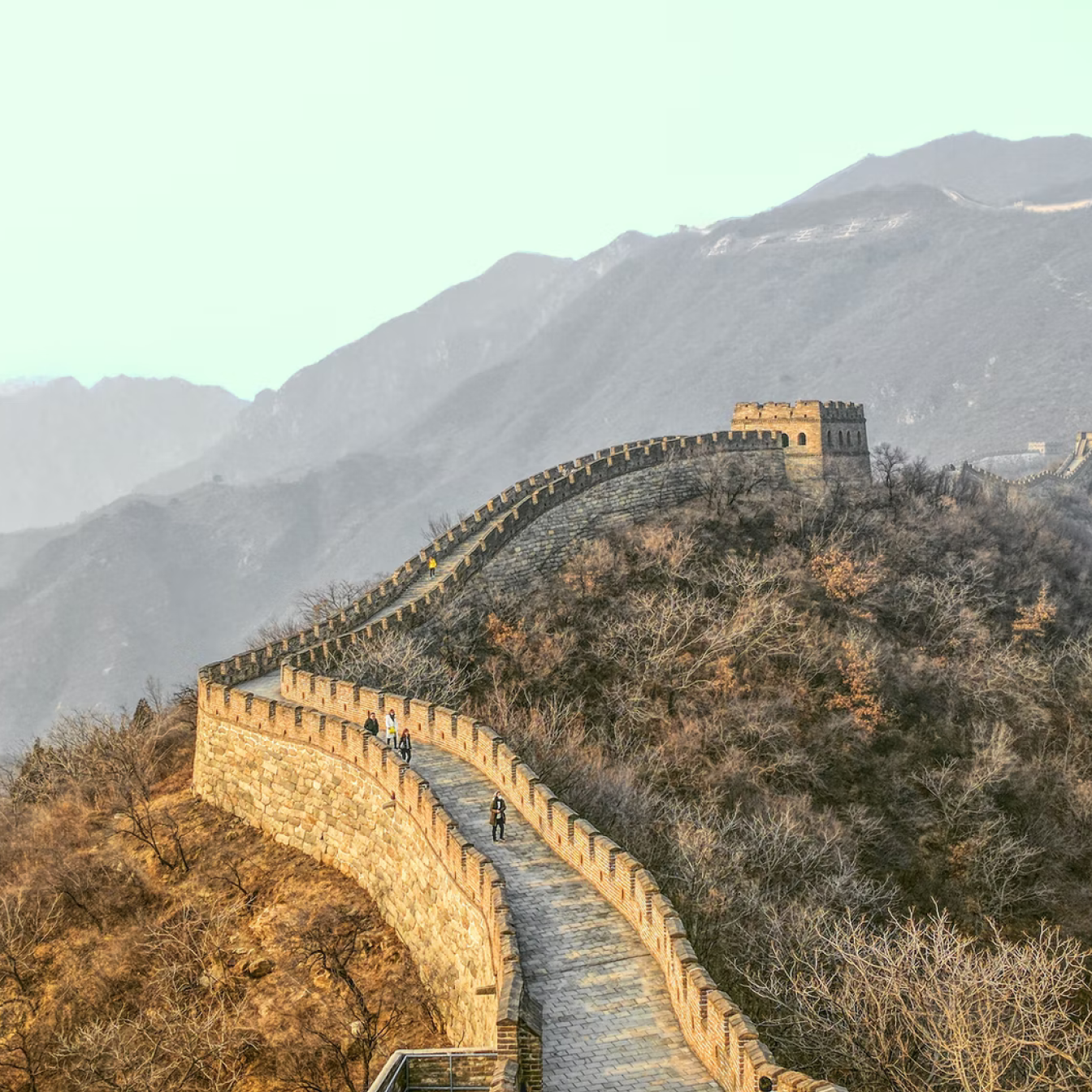 Stunning mountainous landscape surrounding the Great Wall of China, with a portion of the stone wall and a watchtower.