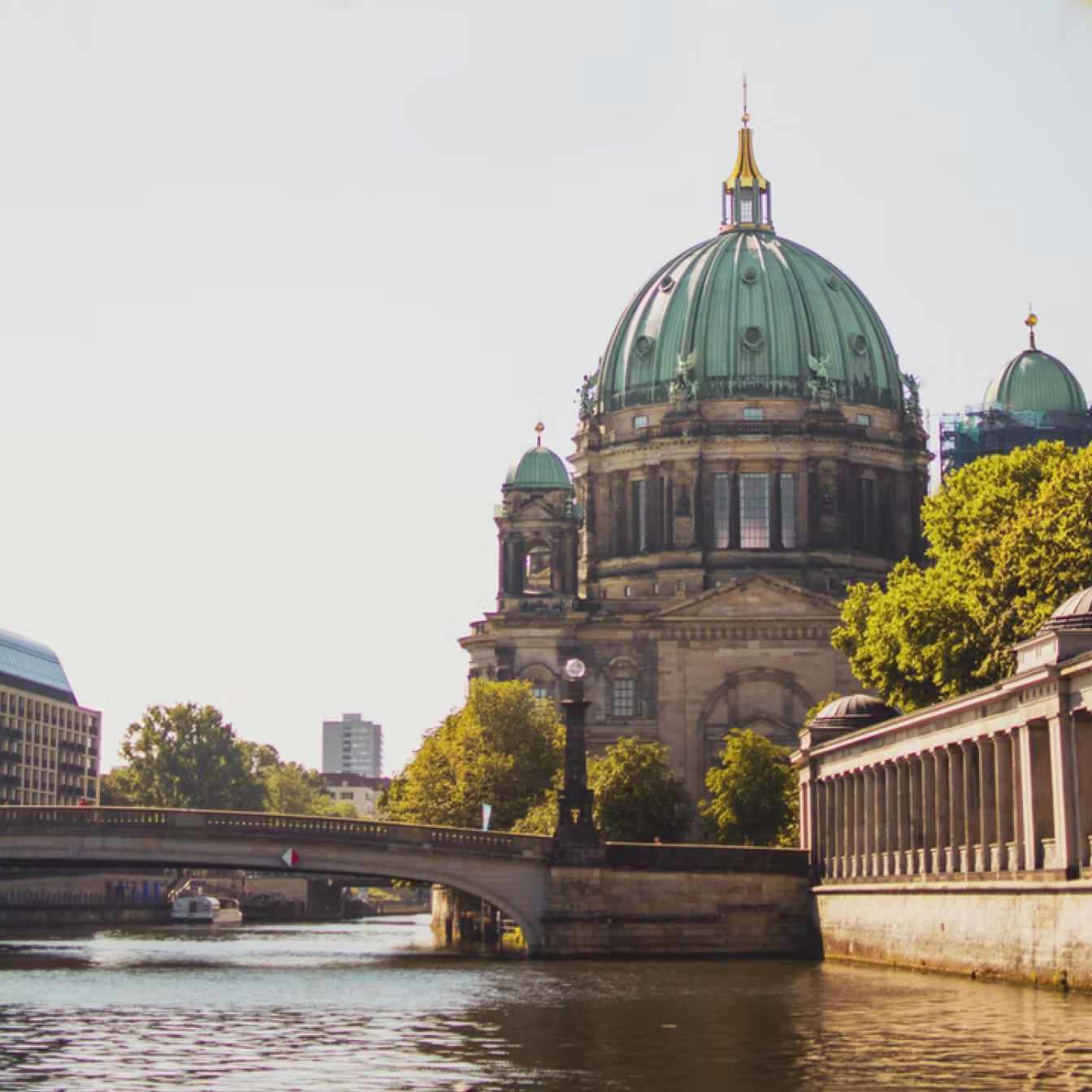 Pretty view of a tree-lined river in Germany, stone bridge and impressive historical building with an oxidised copper dome.