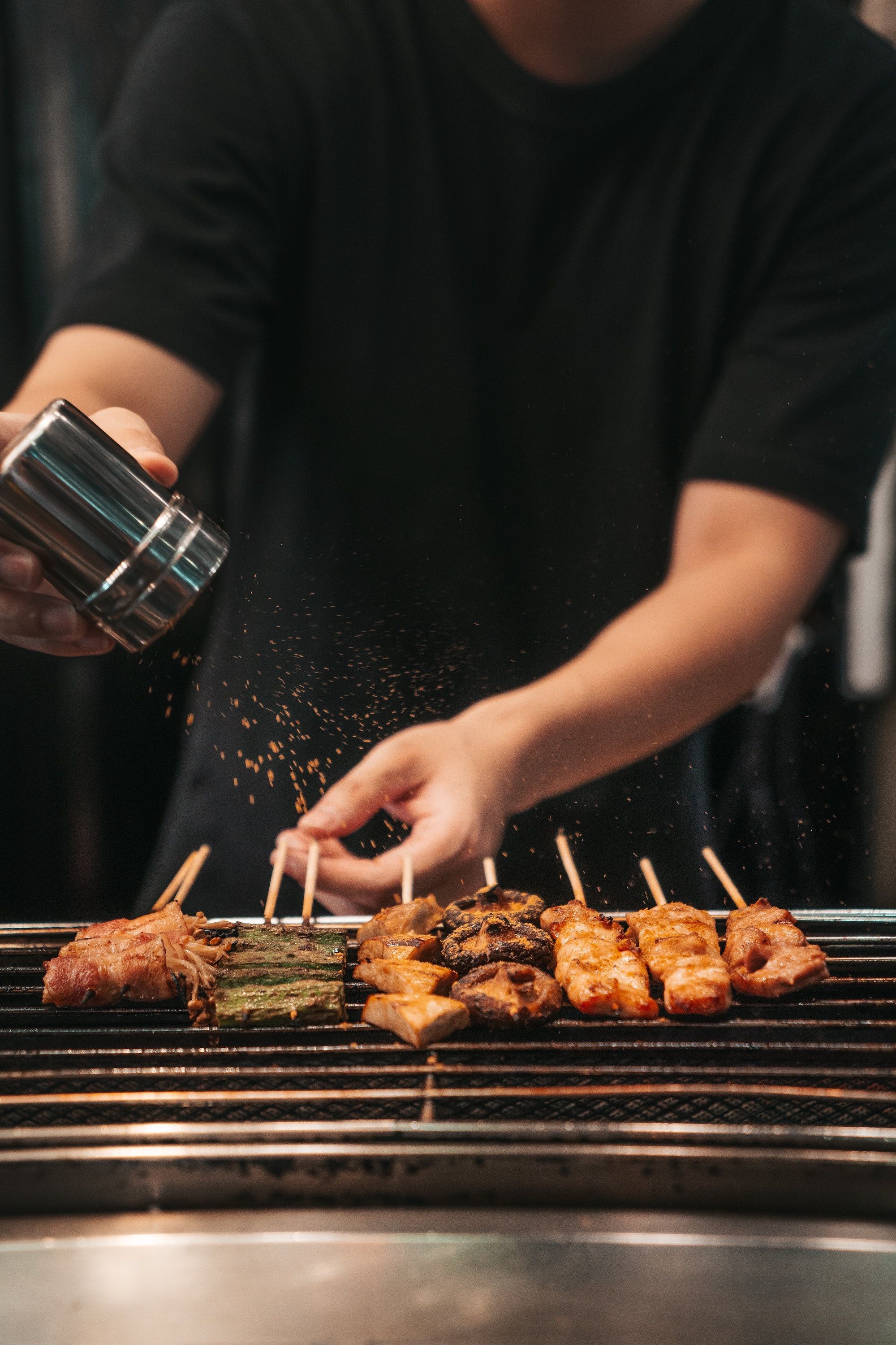 A chef prepares different skewers of meat on an open grill.