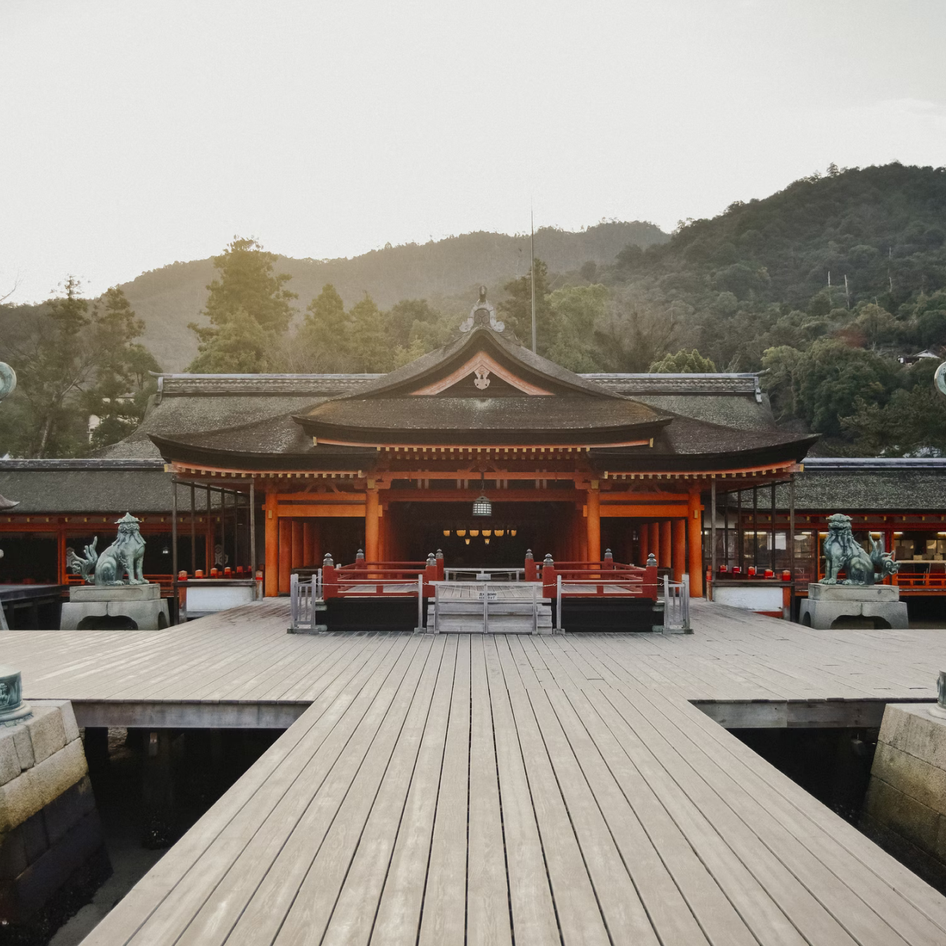 Red wooden Japanese temple in the morning light, surrounded by forest with traditional statues on either side.Red wooden Japanese temple in the morning light, surrounded by forest with traditional statues on either side.
