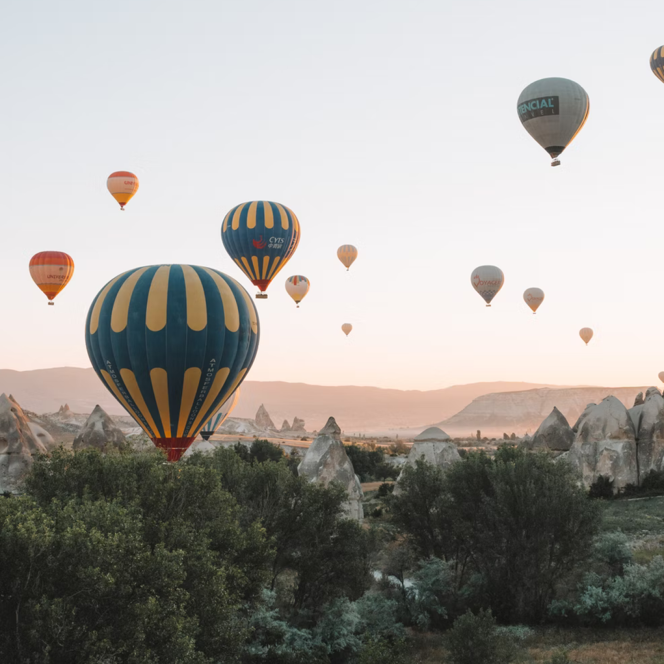 Sunrise over Cappadocia in Türkiye with 12 hot air balloons in the sky above trees and the "fairy chimney" rock formations.Sunrise over Cappadocia in Türkiye with 12 hot air balloons in the sky above trees and the "fairy chimney" rock formations.