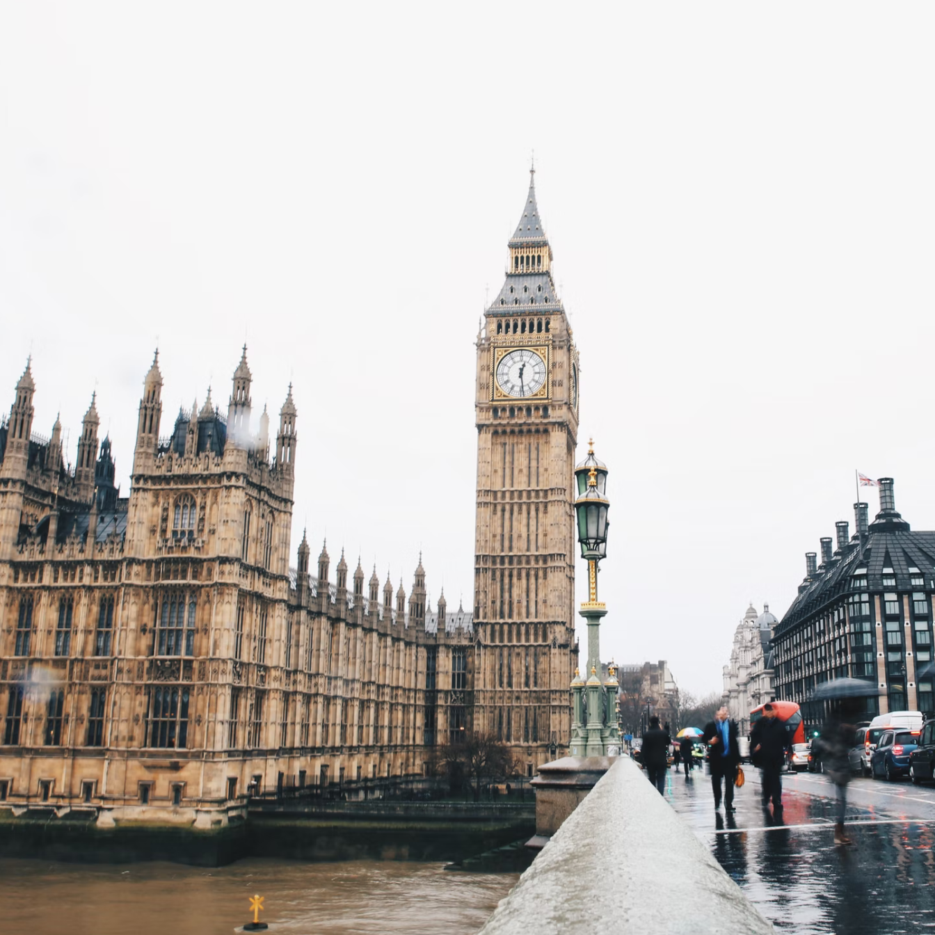 View of the Houses of Parliament and Big Ben clock tower and pedestrians from Westminster Bridge in London on a rainy day.
