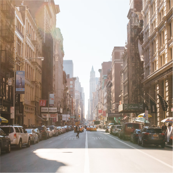 View looking down a typical New York Street with stone buildings, skyscrapers in the distance and yellow taxis on the road.