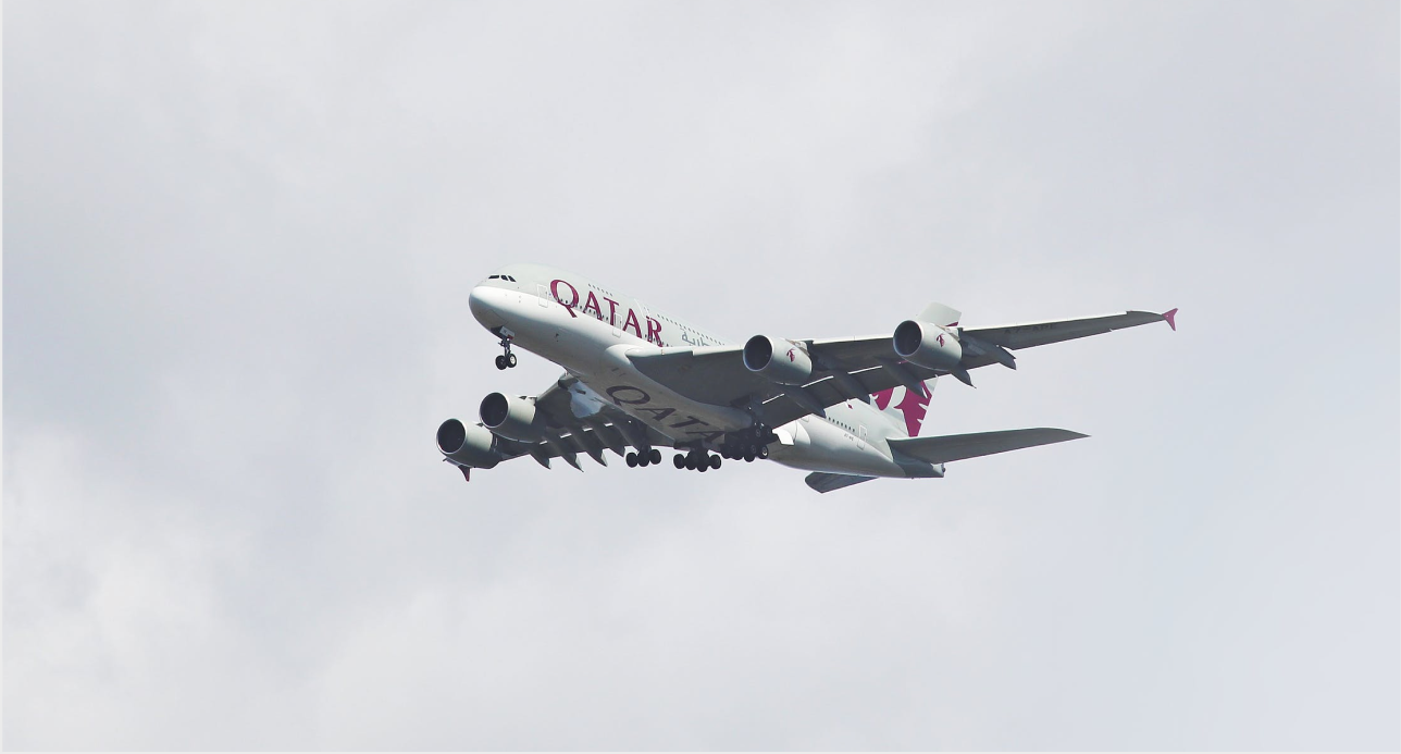 Qatar Airways plane flying in the sky, viewed from below surrounded by clouds.
