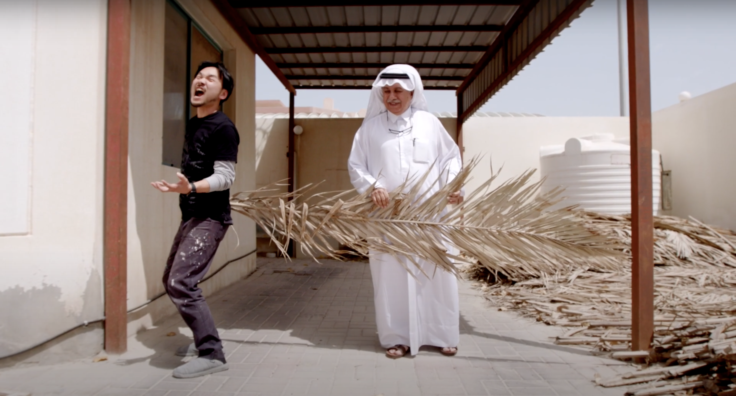 Japanese artist Hayaki Nishigaki and Qatari artist Yousef Ahmad holding a giant palm frond at the artists' studio in Doha.