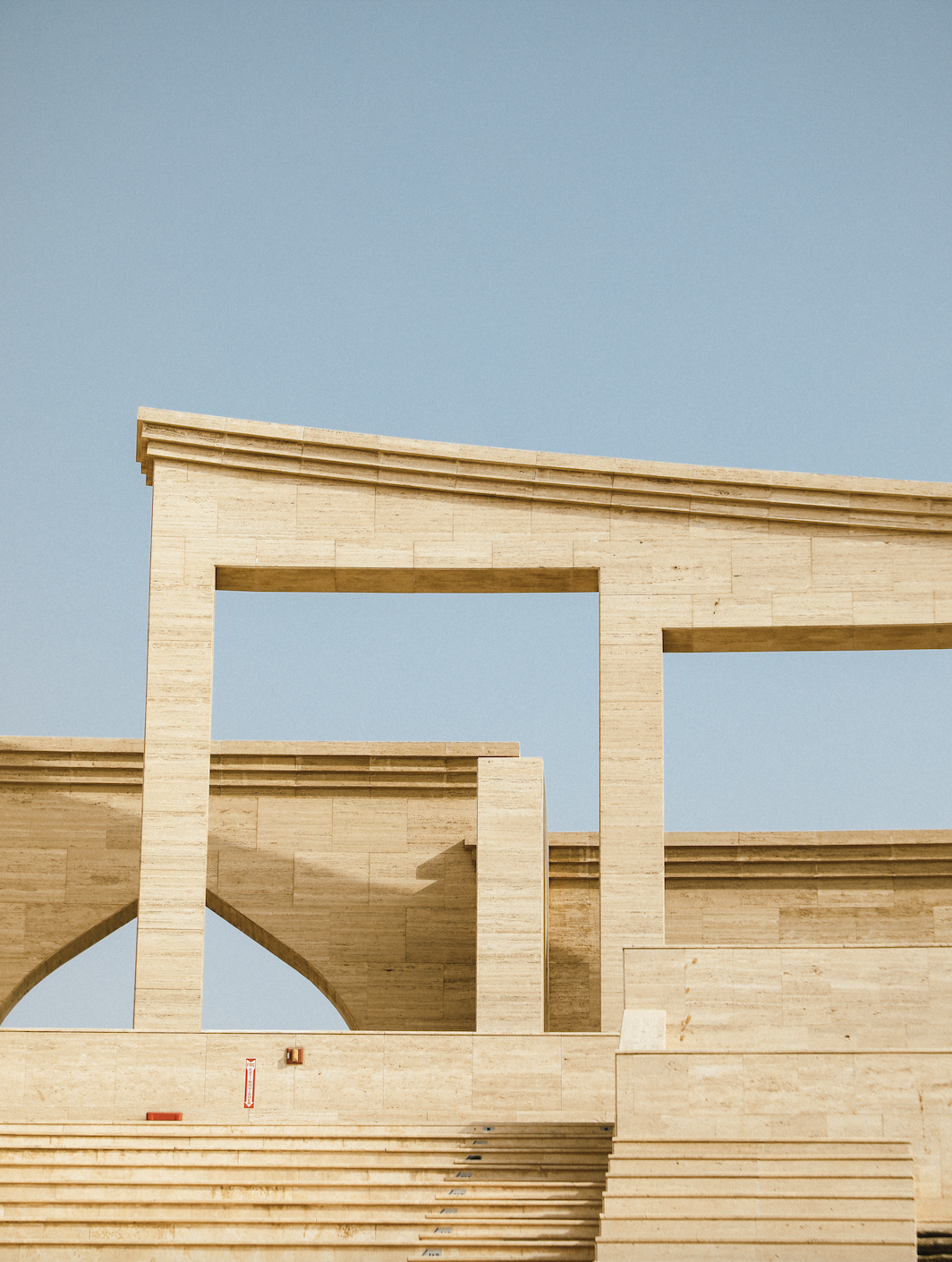 Steps leading up to stone archways at the top of Katara Amphitheatre, silhouetted against a pale blue sky. 