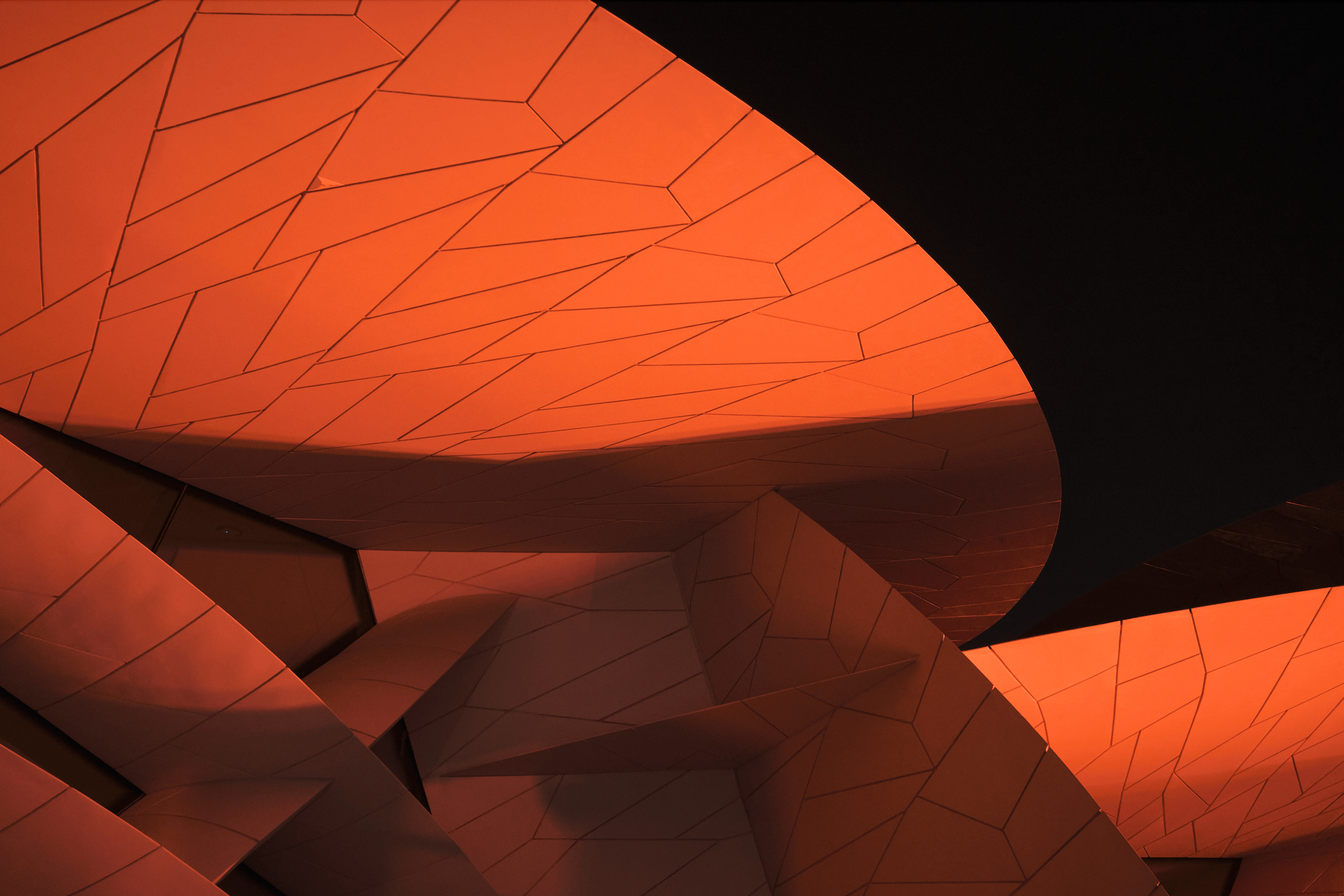 Details of the National Museum of Qatar designed by Jean Nouvel, illuminated from below with red lighting at night.
