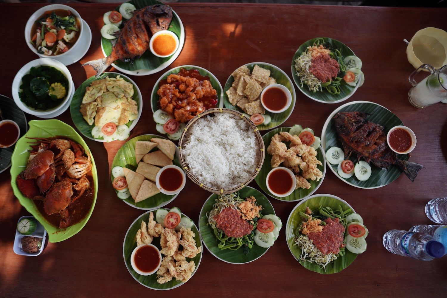 A wooden table seen from above, covered with different plates of traditional Indonesian food.