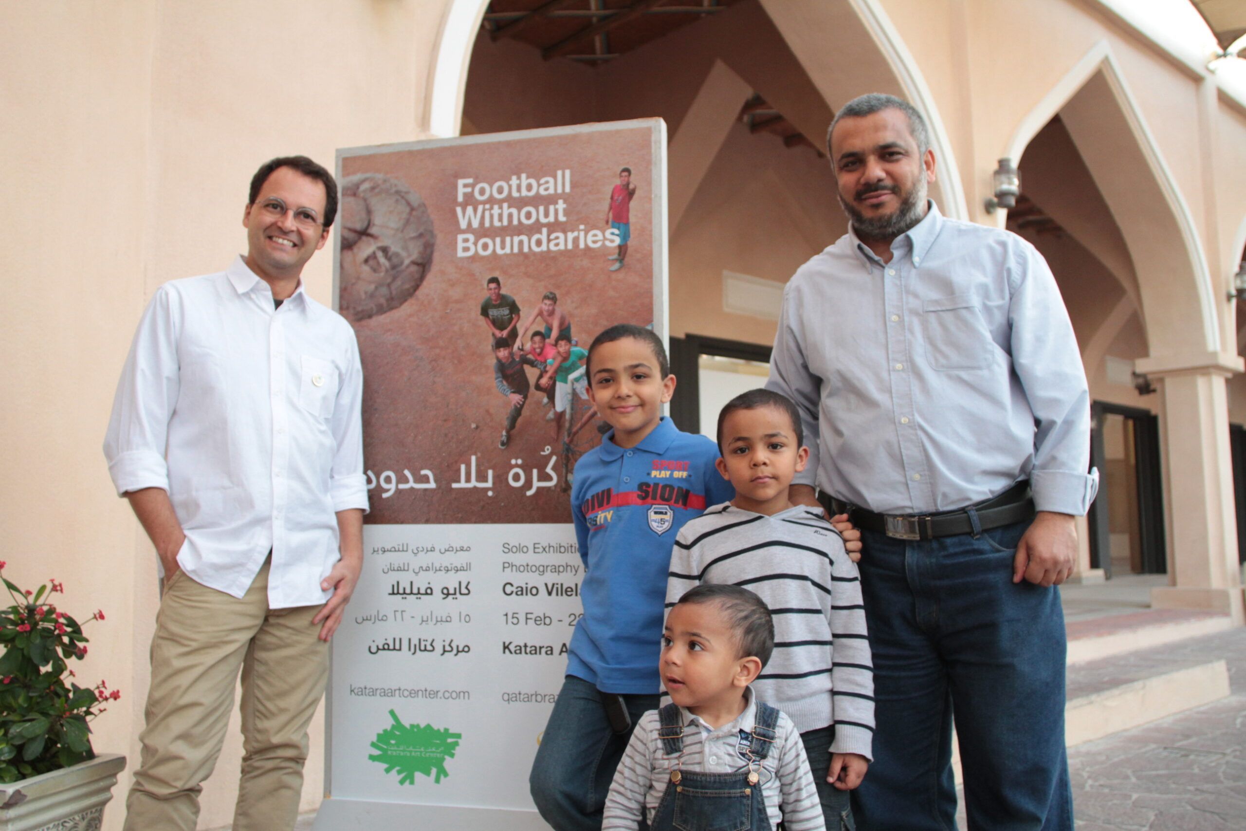 Two men stand with three young boys in front of an information panel at the Football without boundaries exhibition at Katara.