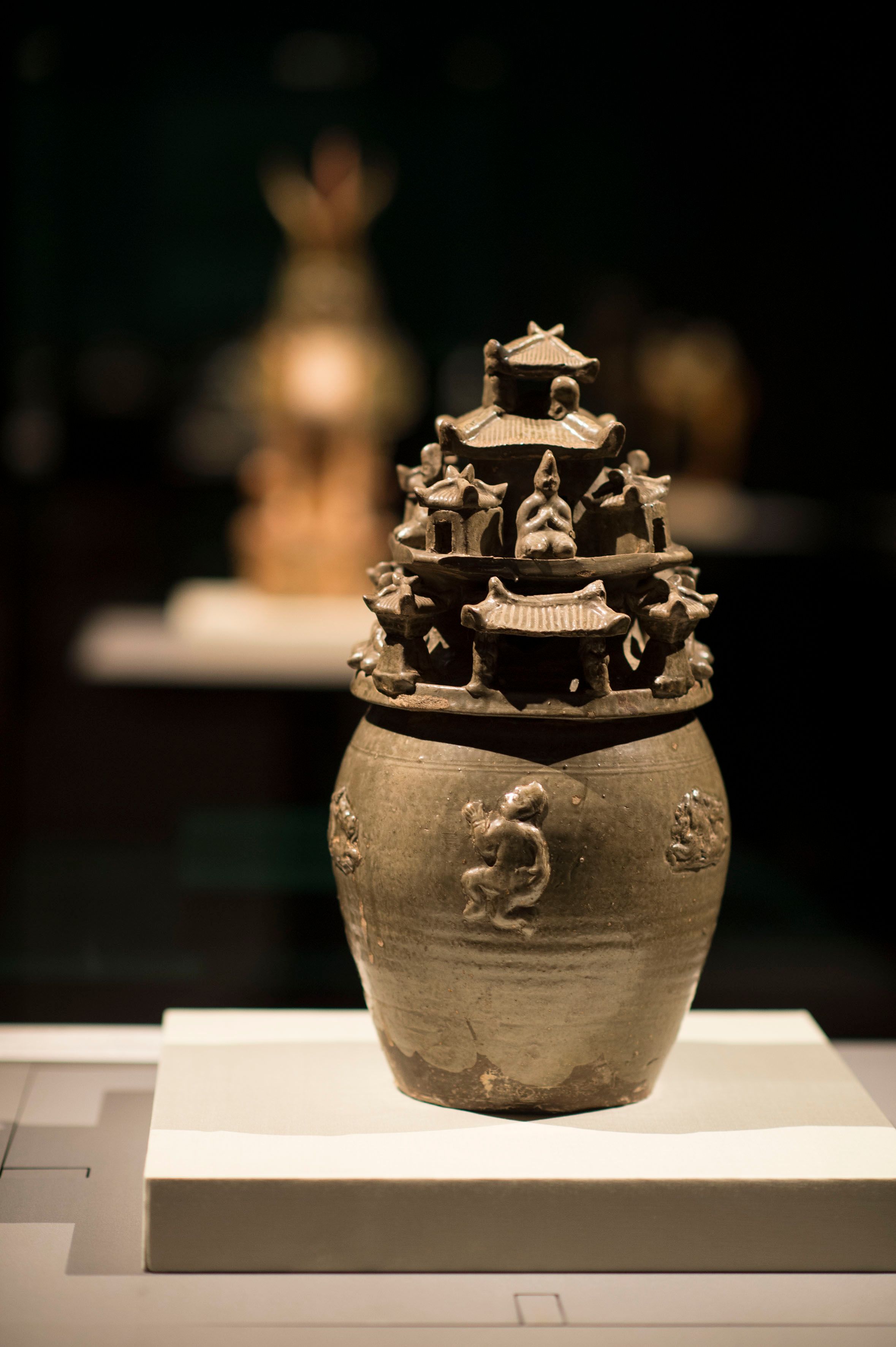 A Chinese ceramic pot and sculpted lid with figures and small Chinese buildings, part of the Treasures of China exhibition.