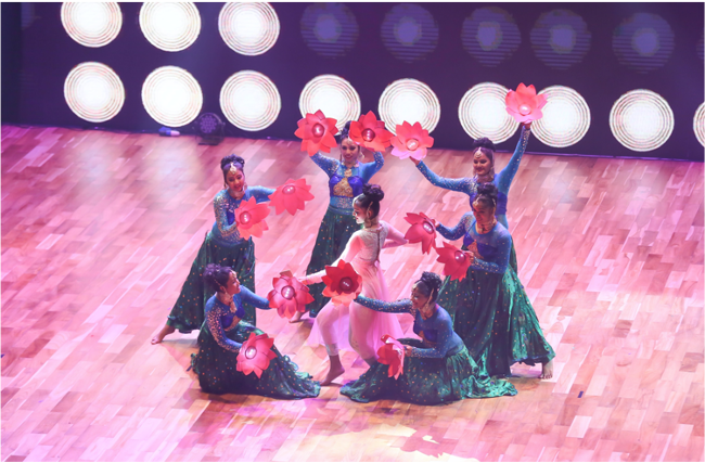 Indian dancers wearing green dresses dance in a circle during a performance of Ticket To Bollywood - An Indian Bioscope.