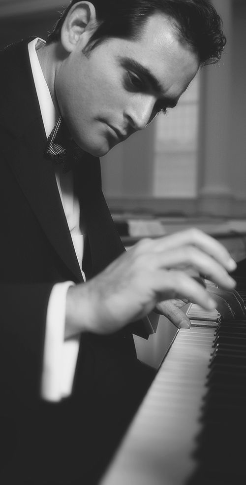 Syrian composer Malek Jandali playing the keys of a piano wearing a black tuxedo, in black and white.