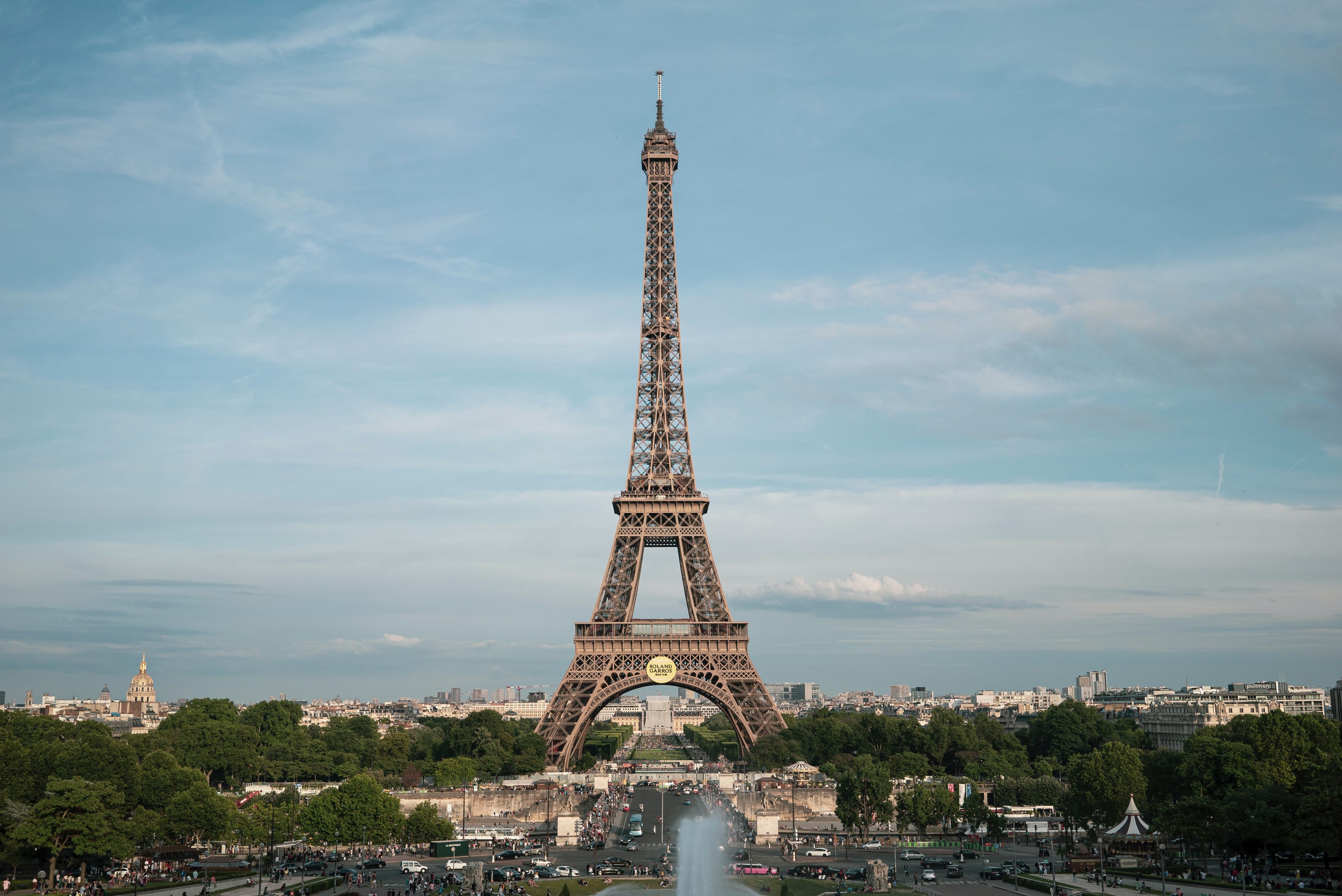 The Eiffel Tower seen from a distance against a blue sky, with the skyline of Paris in the background.