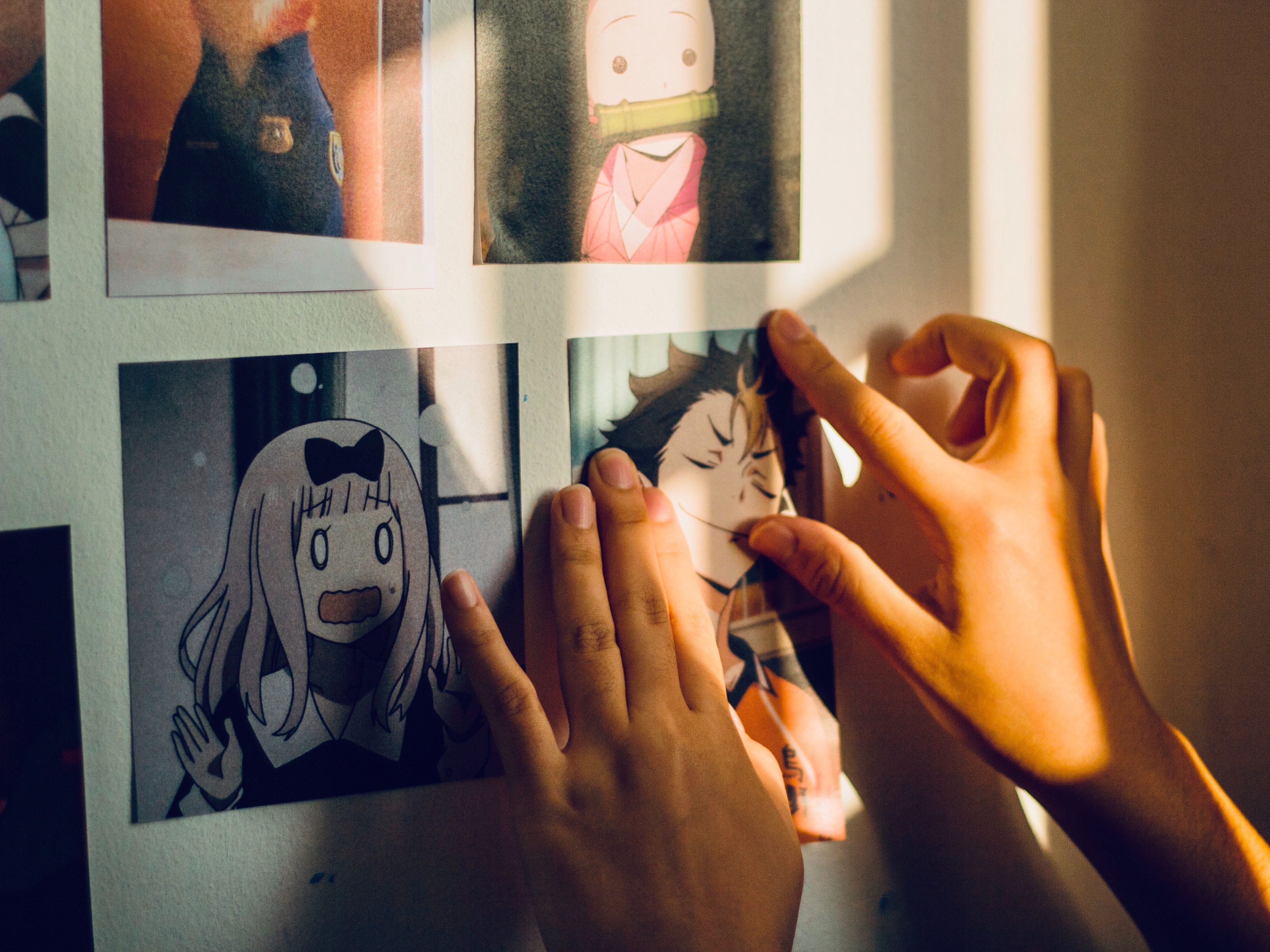 Two hands holding a printed manga cartoon up to a wall, beside a collage of different printed manga illustrations.Two hands holding a printed manga cartoon up to a wall, beside a collage of different printed manga illustrations.