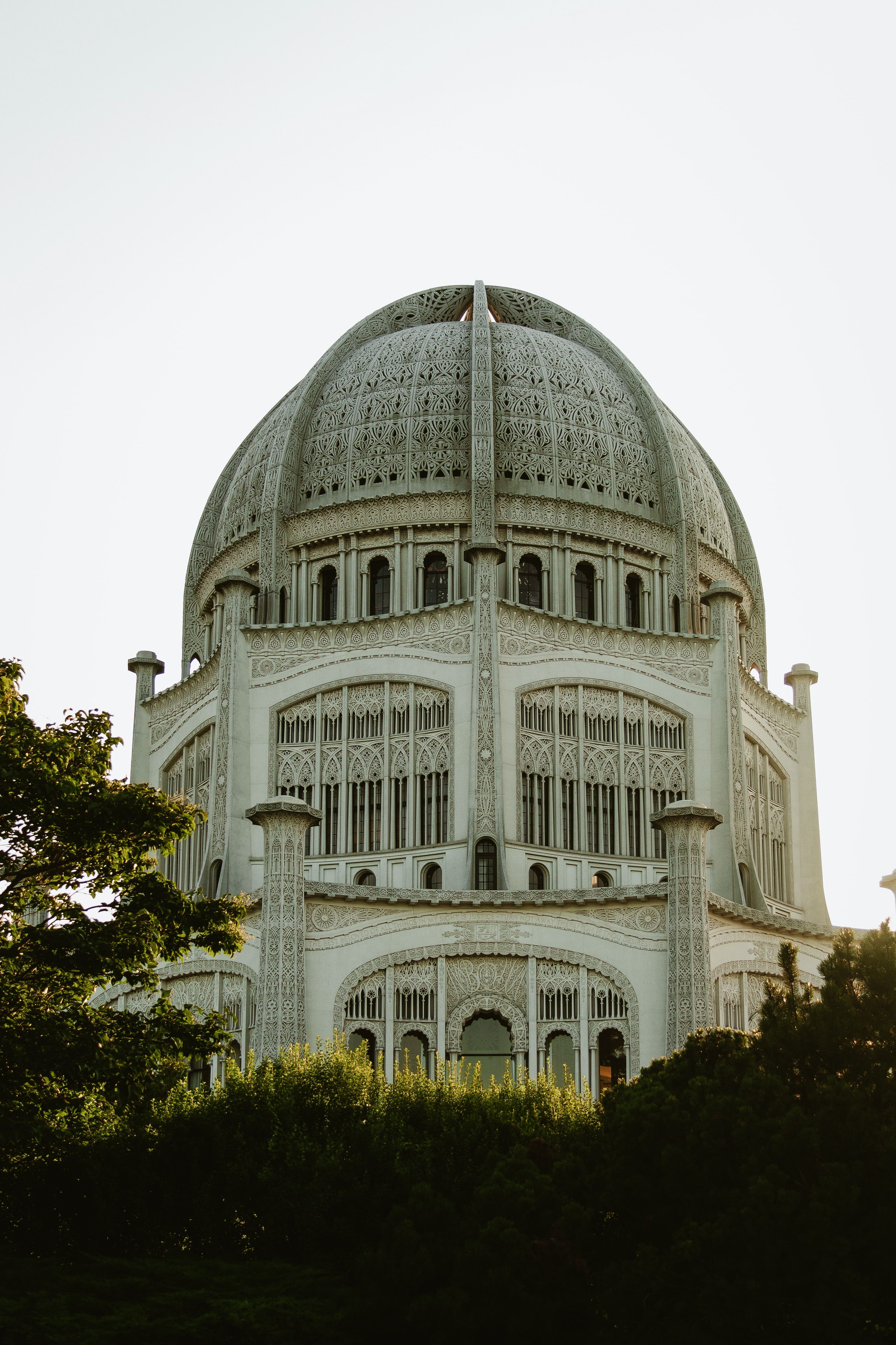 A domed stone tower with ornate patterns and windows surrounded by greenery.