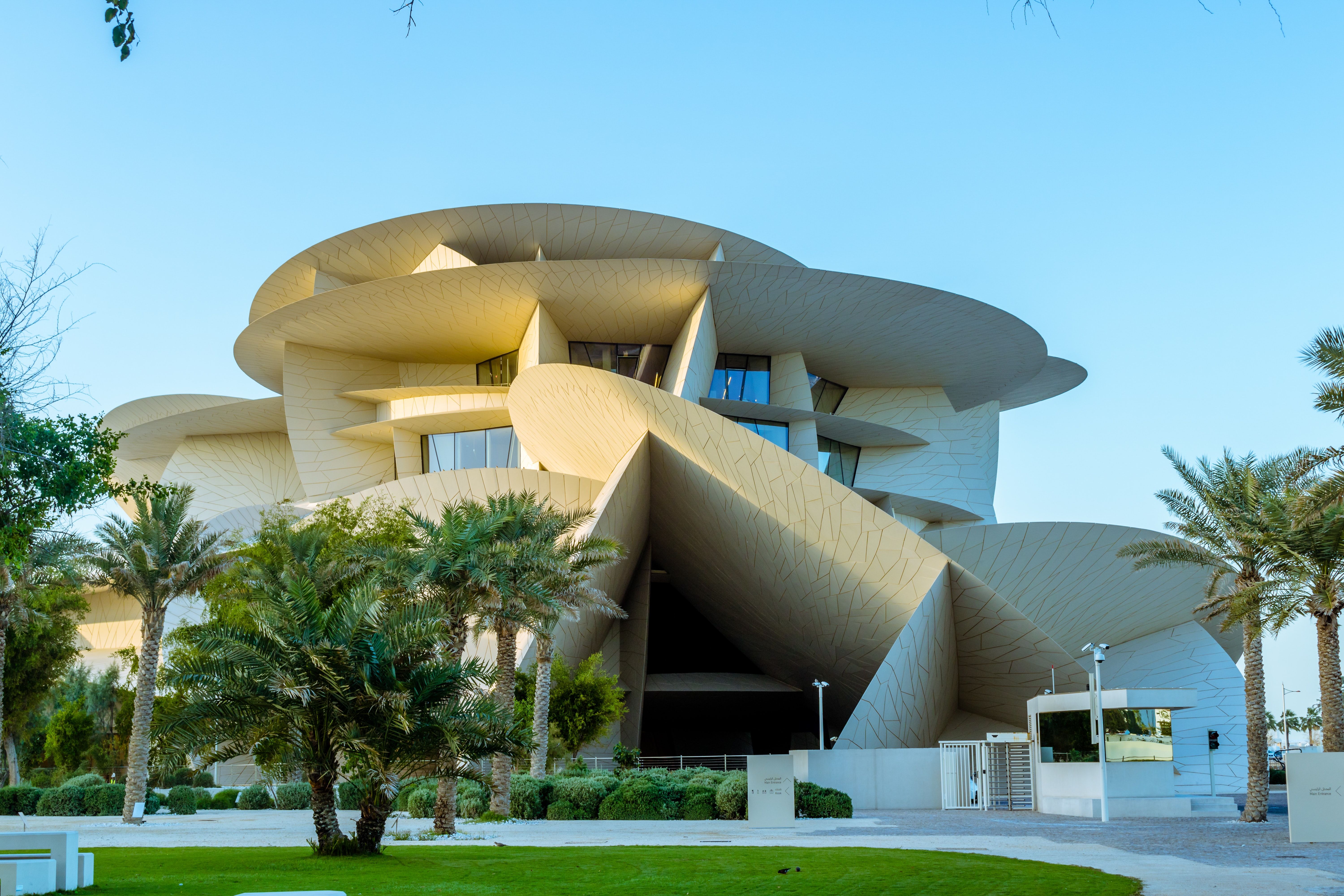 The National Museum of Qatar in Doha on a bright sunny day, with grass and palm trees in the foreground.