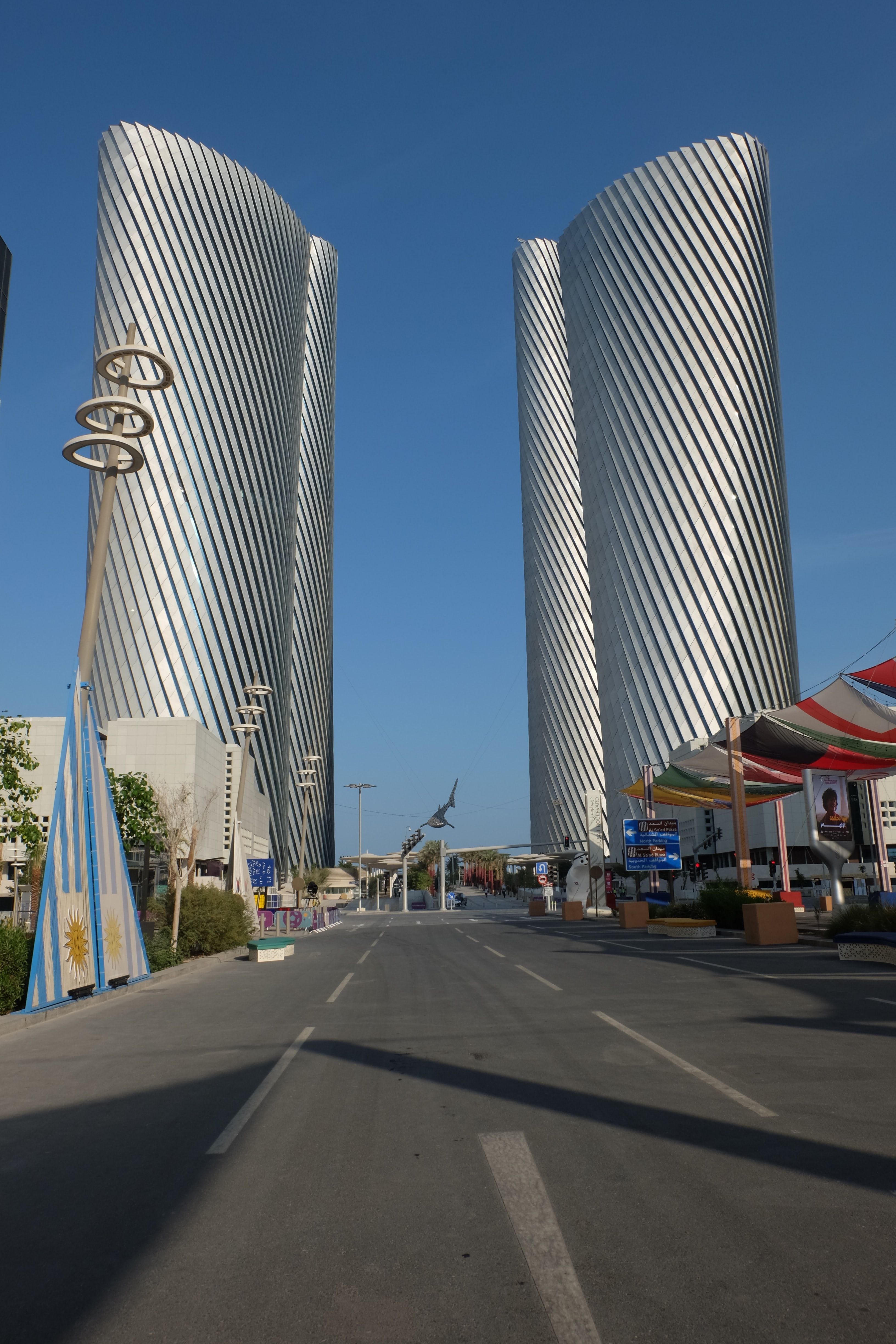Lusail Boulevard in Qatar with two tall silver towers on either side of the road, against a blue sky.